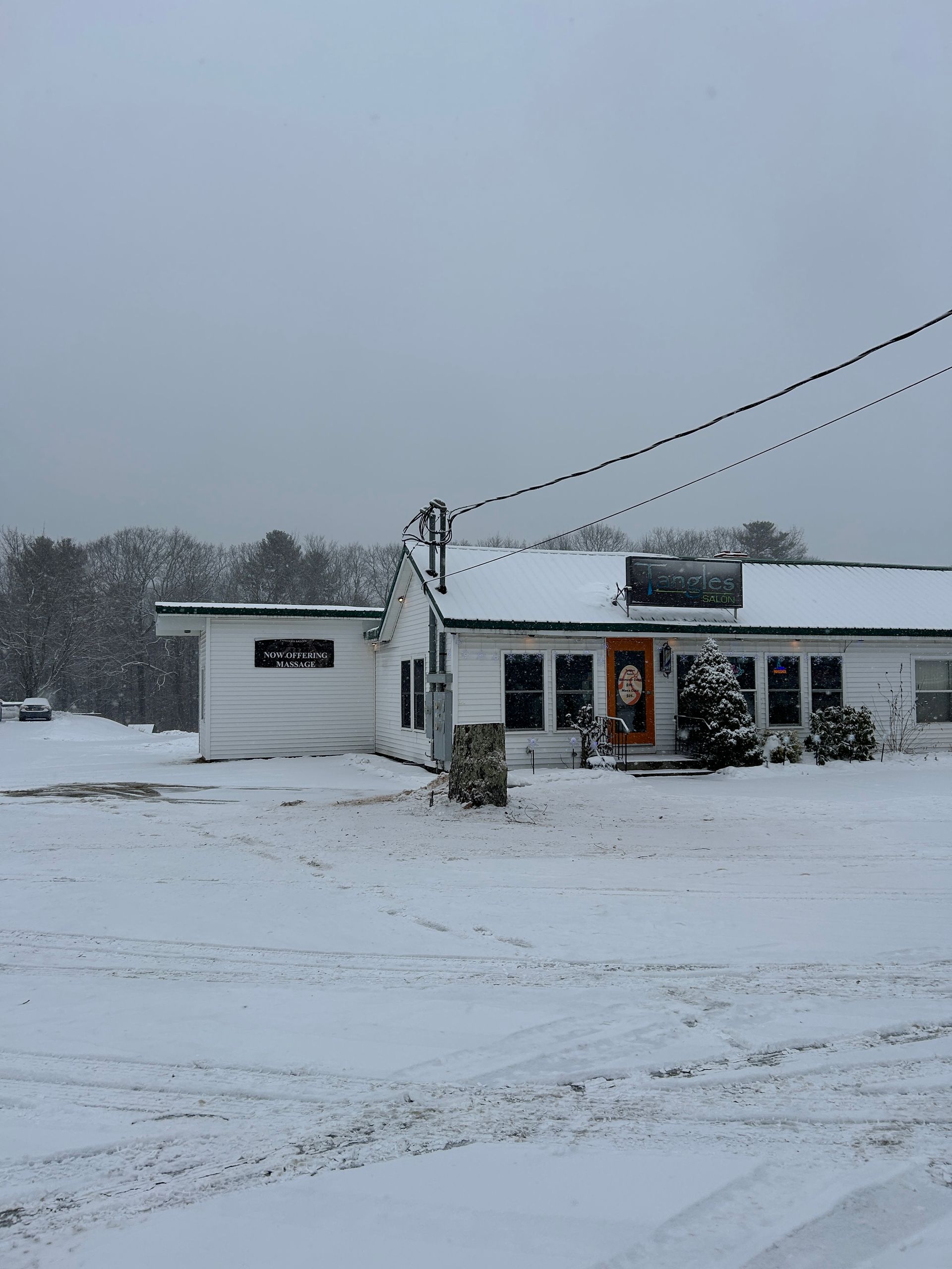 Snow-covered roadside building with a parked car under a gray winter sky