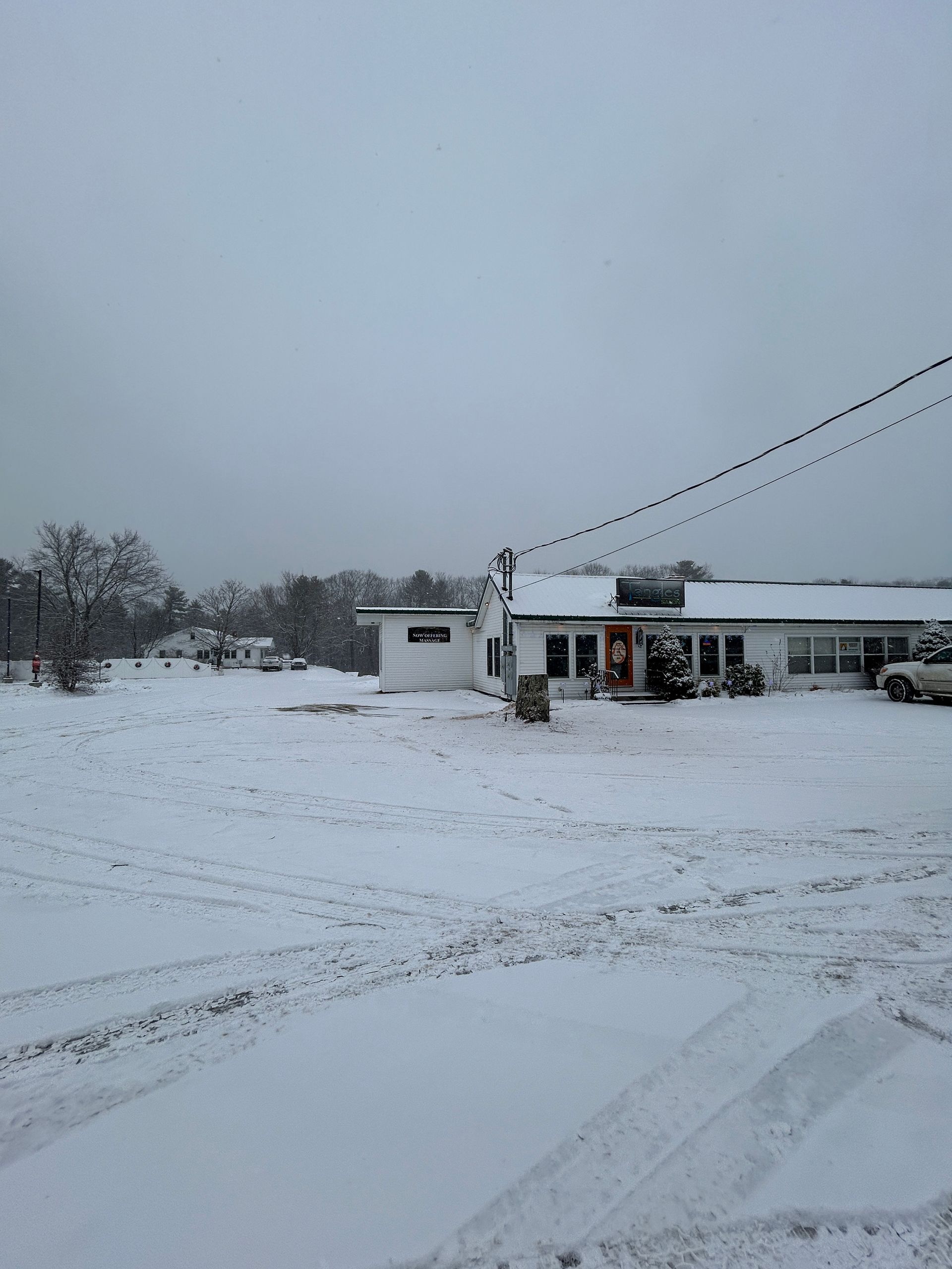 Snowy roadside building with a white truck and tire tracks under an overcast sky