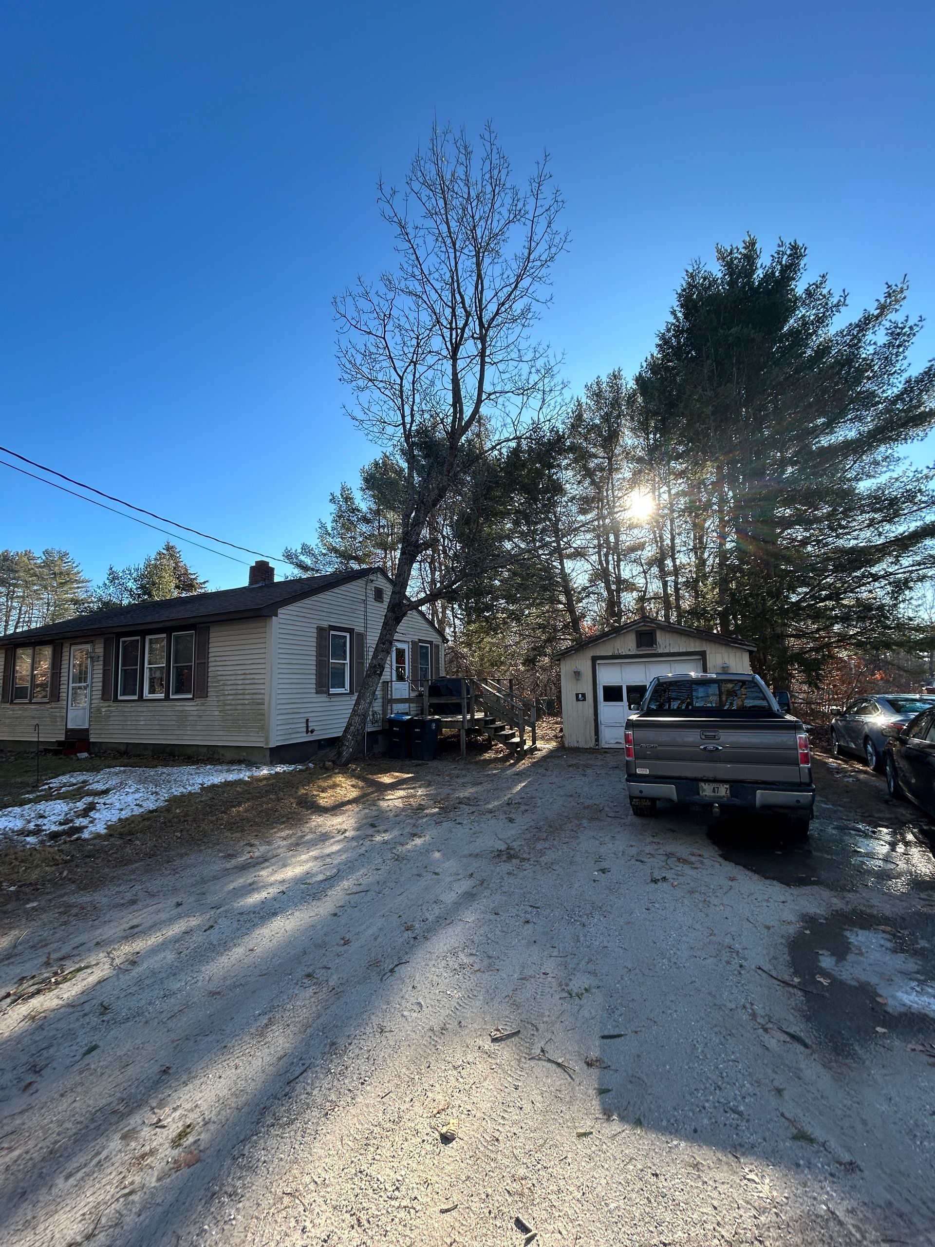 Snowy driveway beside a mobile home and garage, with a pickup truck in bright winter sunlight.