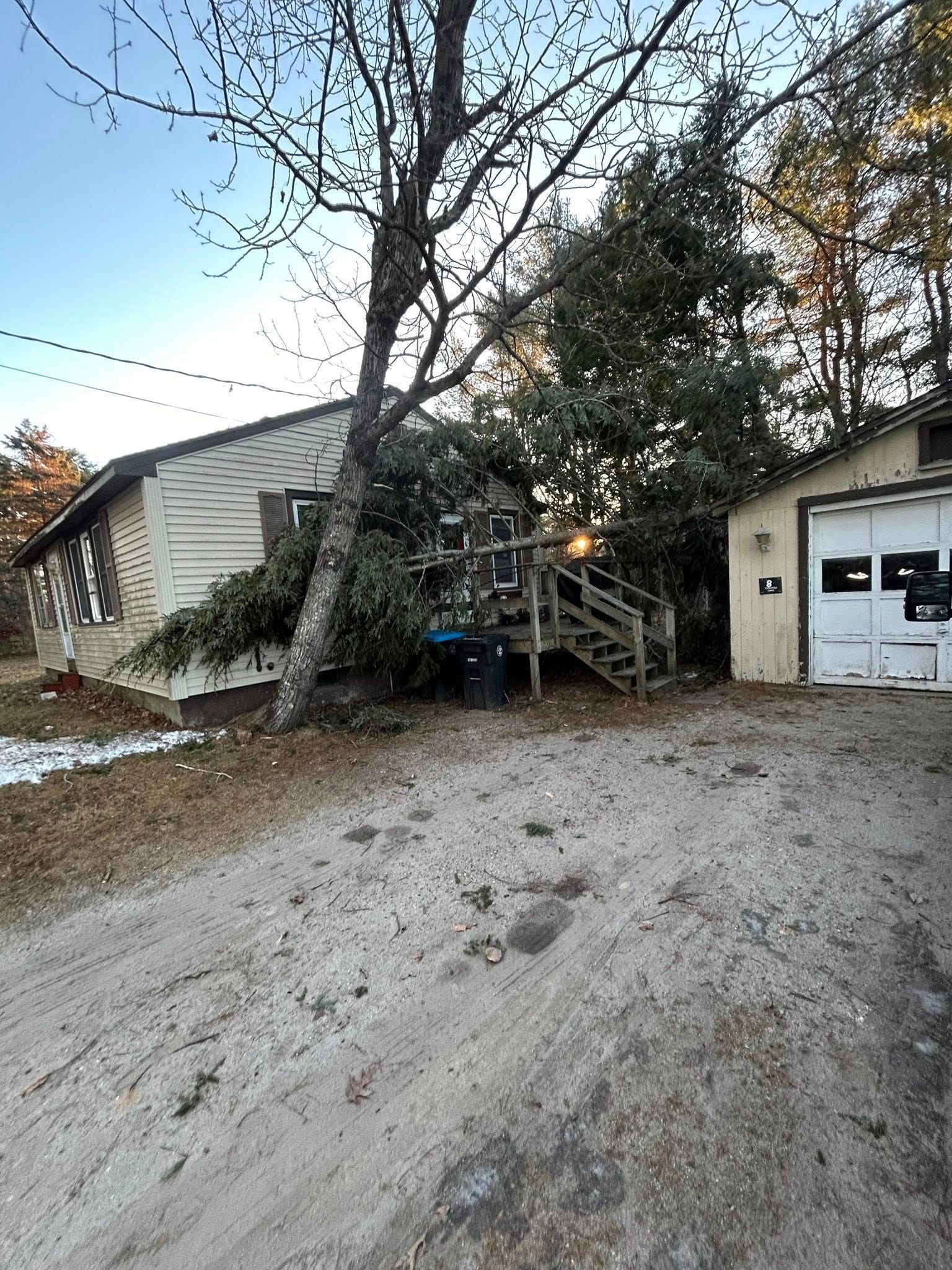 Gravel driveway leading to a beige house with a staircase and white garage under leafless trees at dusk