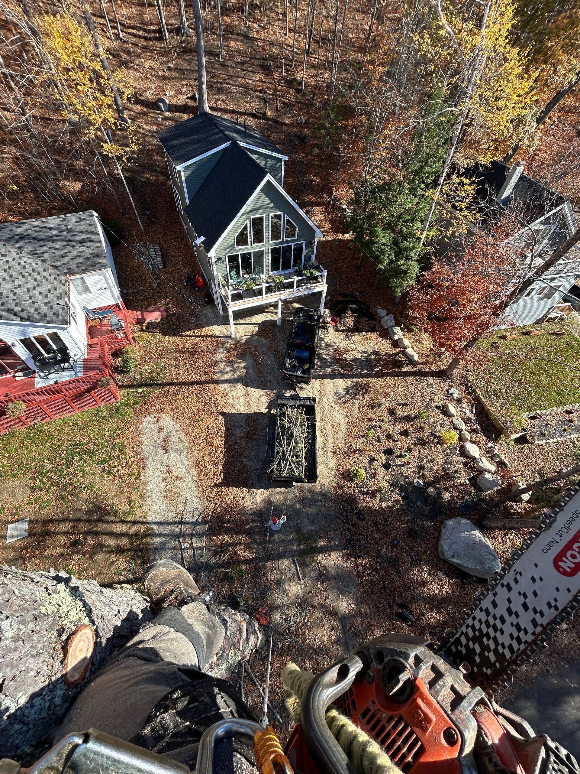 Aerial view of a house and yard in autumn, with a chainsaw in the foreground.