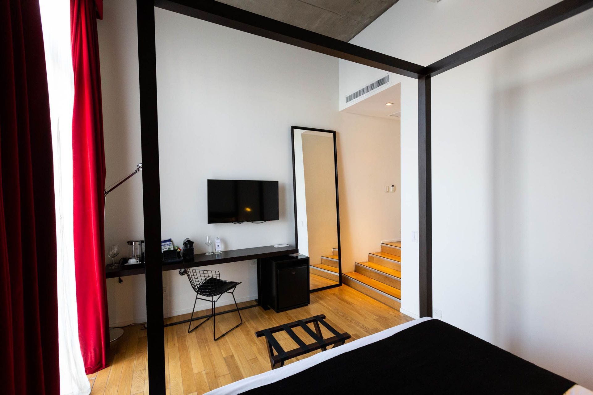 Una habitación de hotel con cama con dosel, escritorio, televisión y espejo.