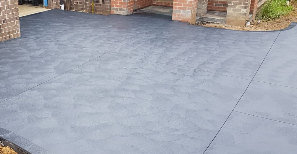 Stamped concrete patio beside a brick house, with a wet gray surface and outdoor steps in view