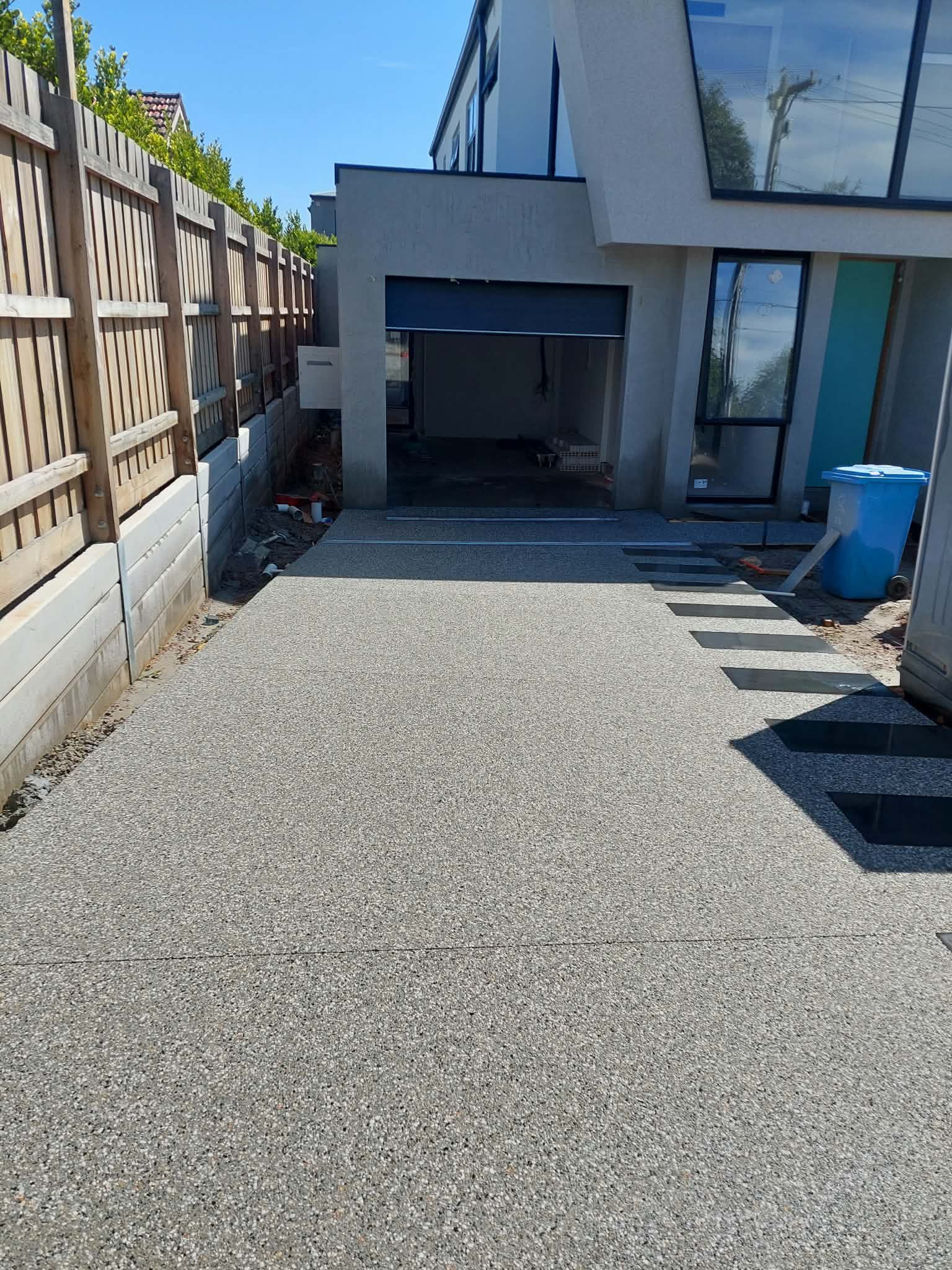 Gravel patio beside a modern house with a covered outdoor fireplace and blue chairs, bordered by a wooden fence