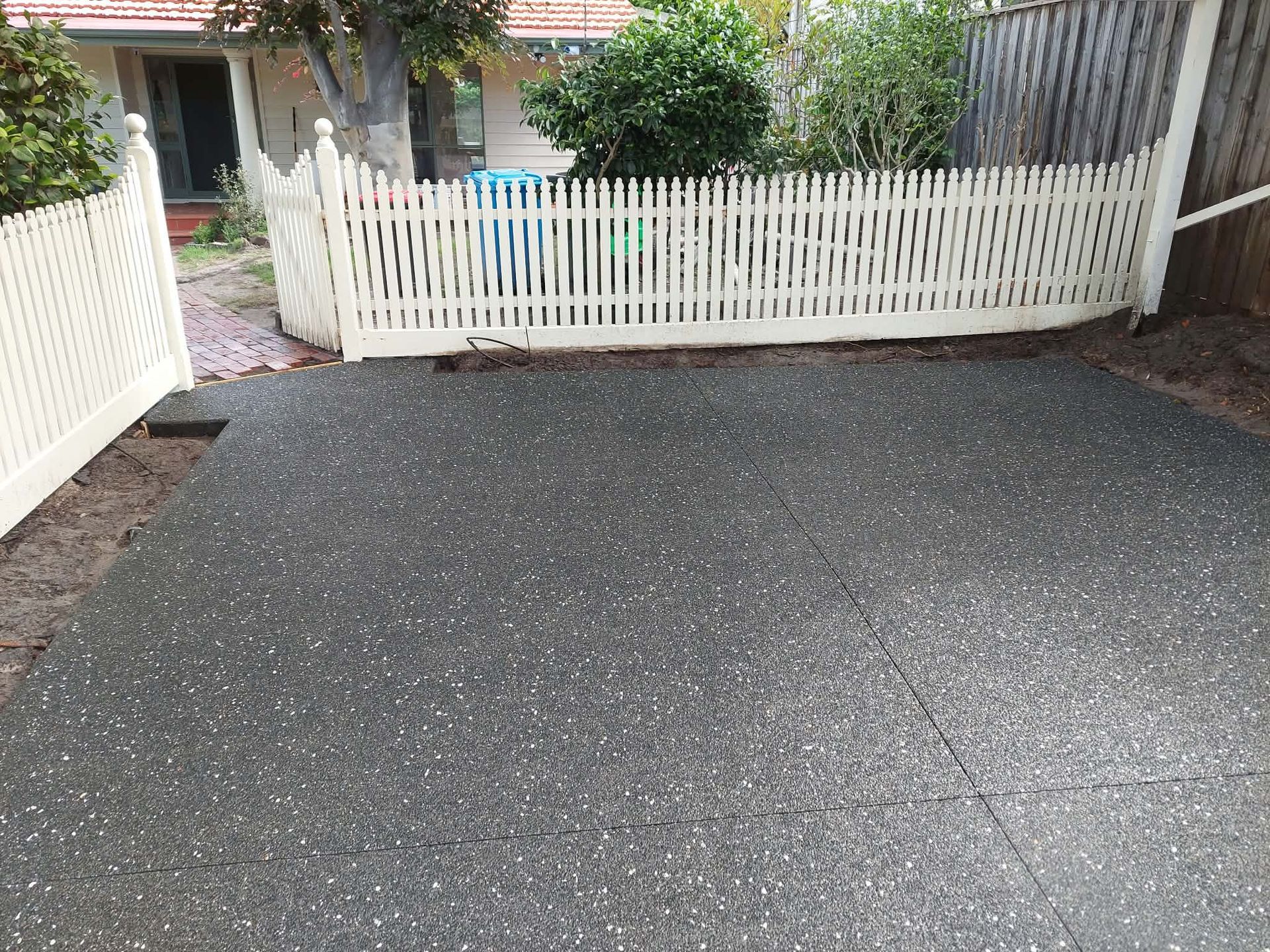 Driveway with fresh dark gravel leading to a white picket gate and house entrance.