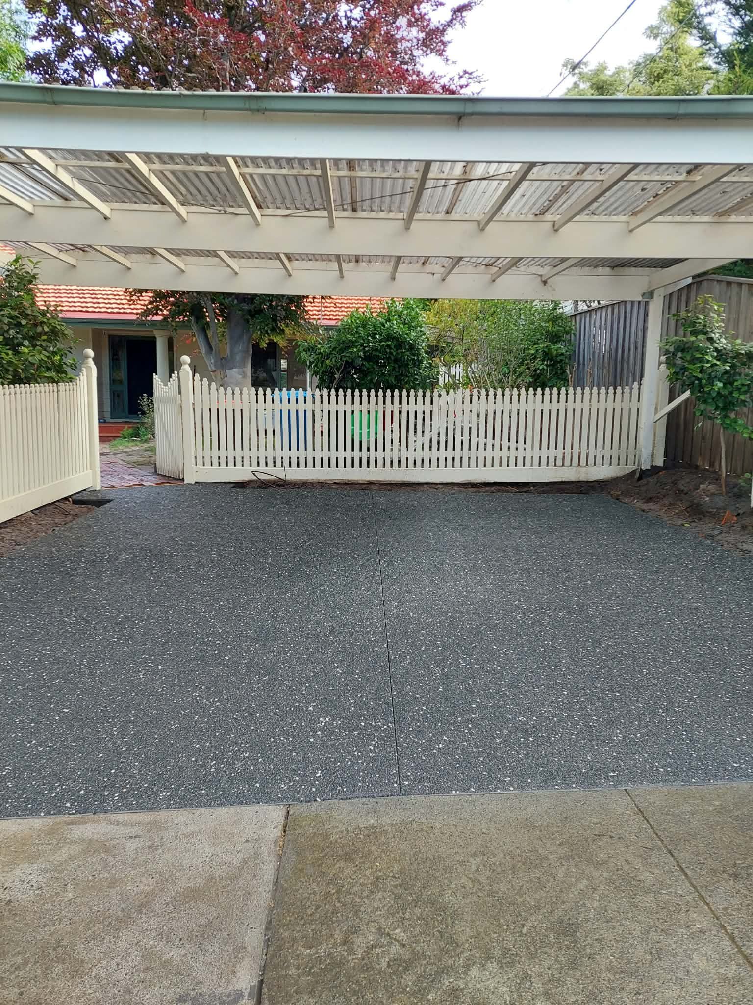 White pergola and picket fence over a gravel driveway, with a house entry in the background.