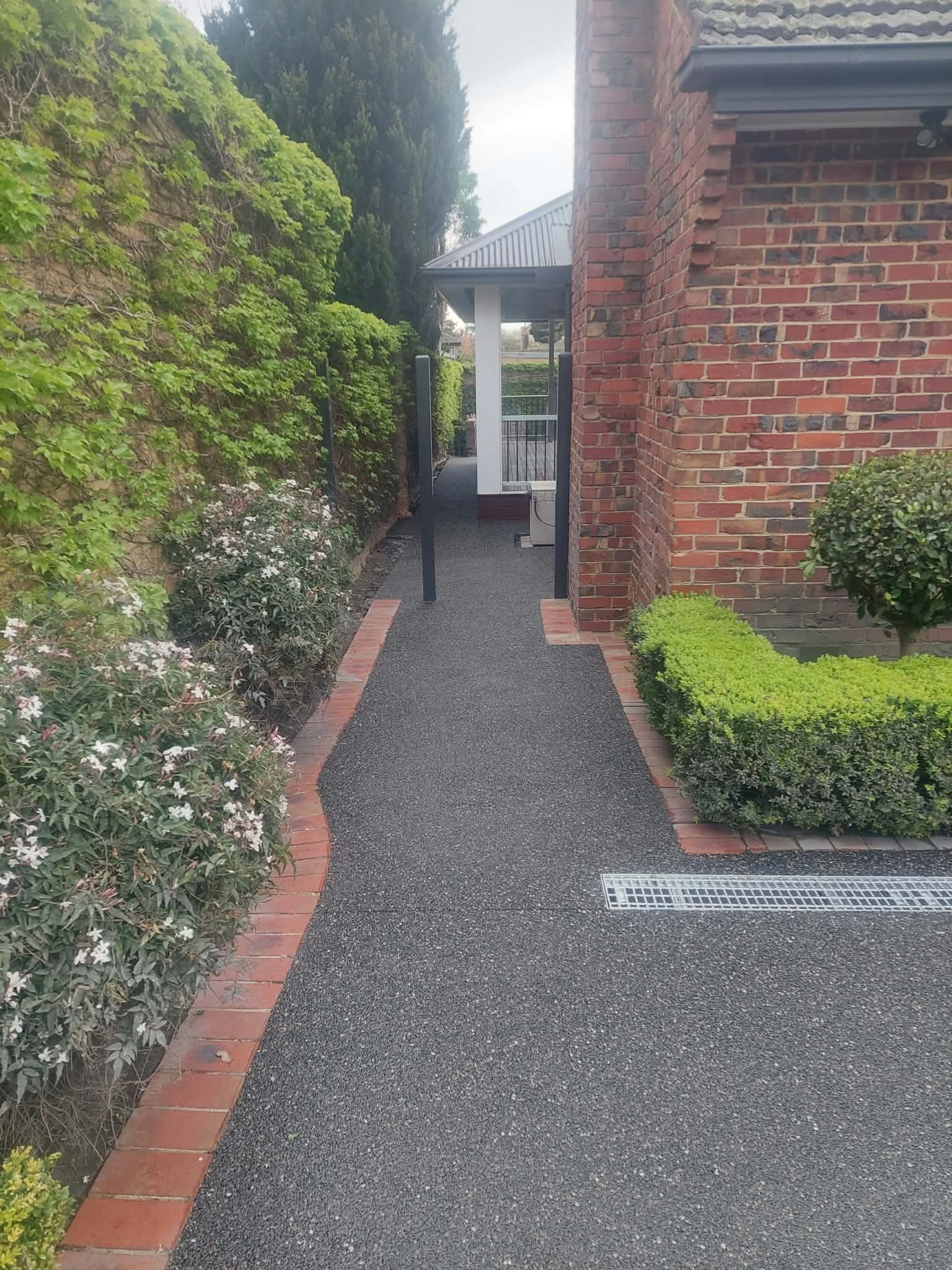 Narrow gravel path between brick walls and hedges leading to a covered entryway