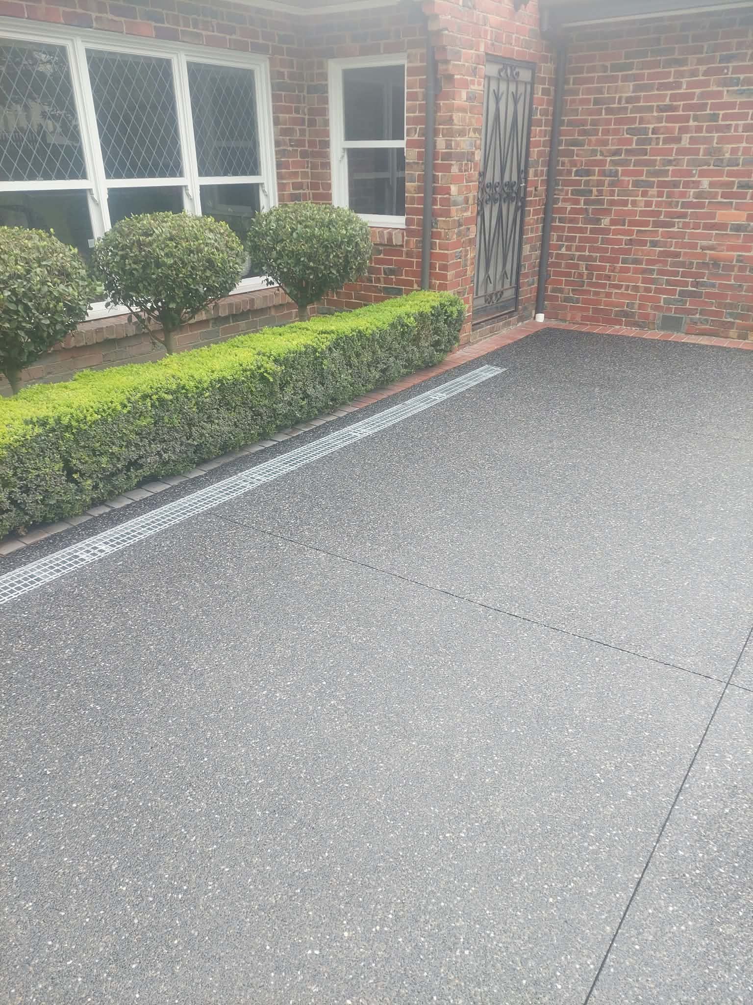 Brick house front entrance with windows, shrubs, and a paved driveway in wet weather