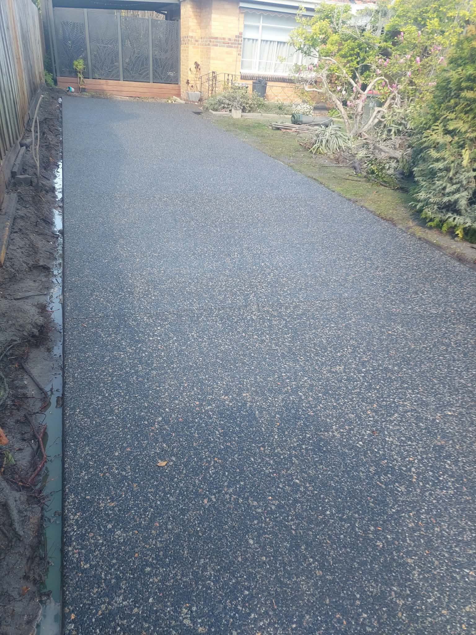 Gravel driveway leading to a closed gate beside hedges and a house