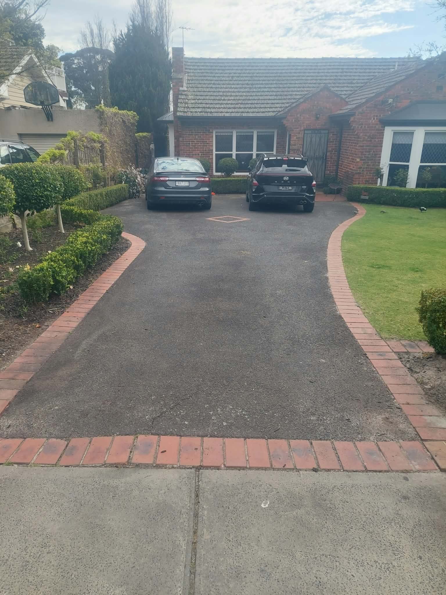 Driveway with two parked cars leading to a suburban house and front lawn.