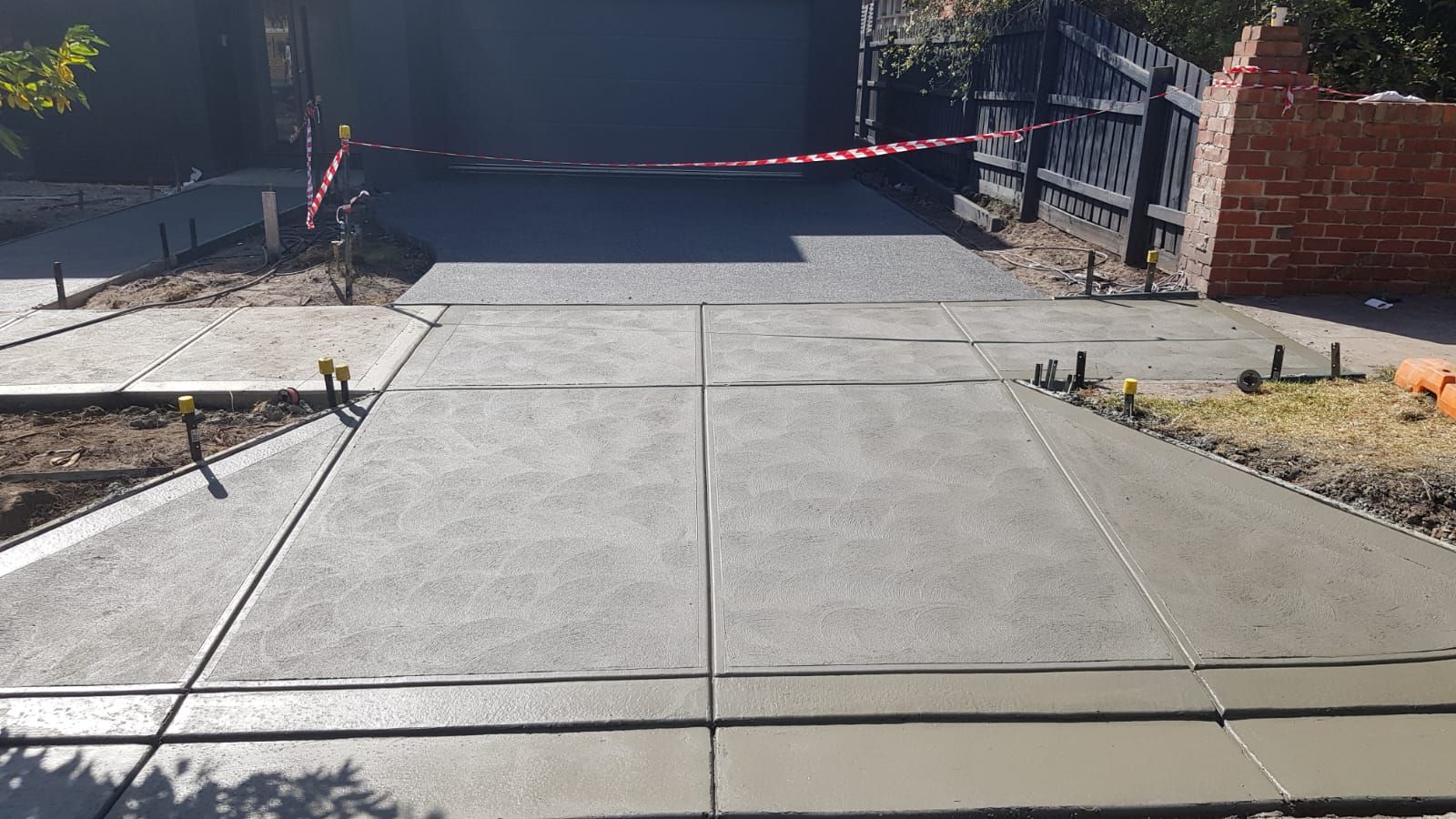 Concrete driveway under construction, blocked by caution tape with tools and debris on both sides.