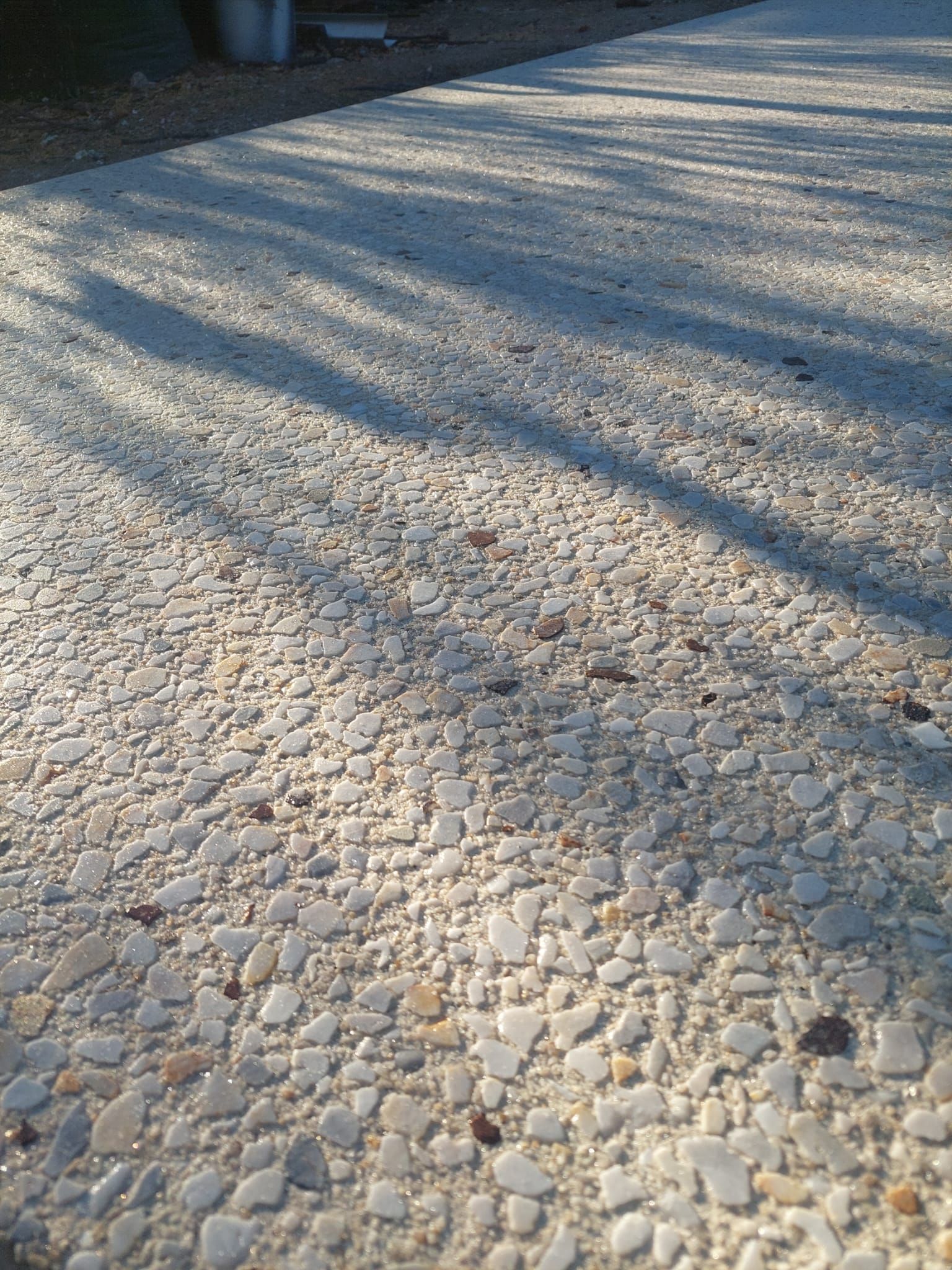 Rocky gravel ground with long tree shadows in bright sunlight