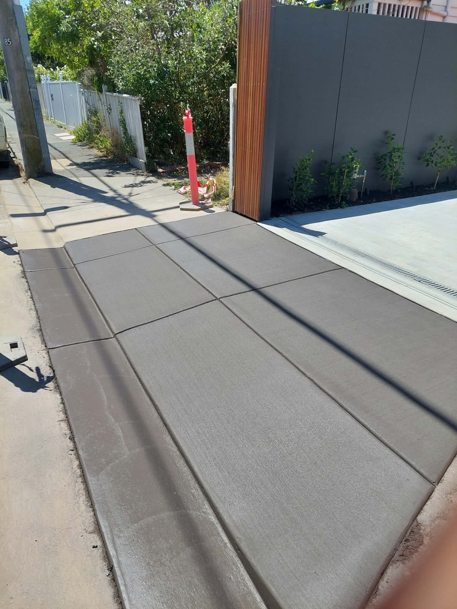 Residential sidewalk with tactile paving, a red post, and a modern gray wall beside a driveway