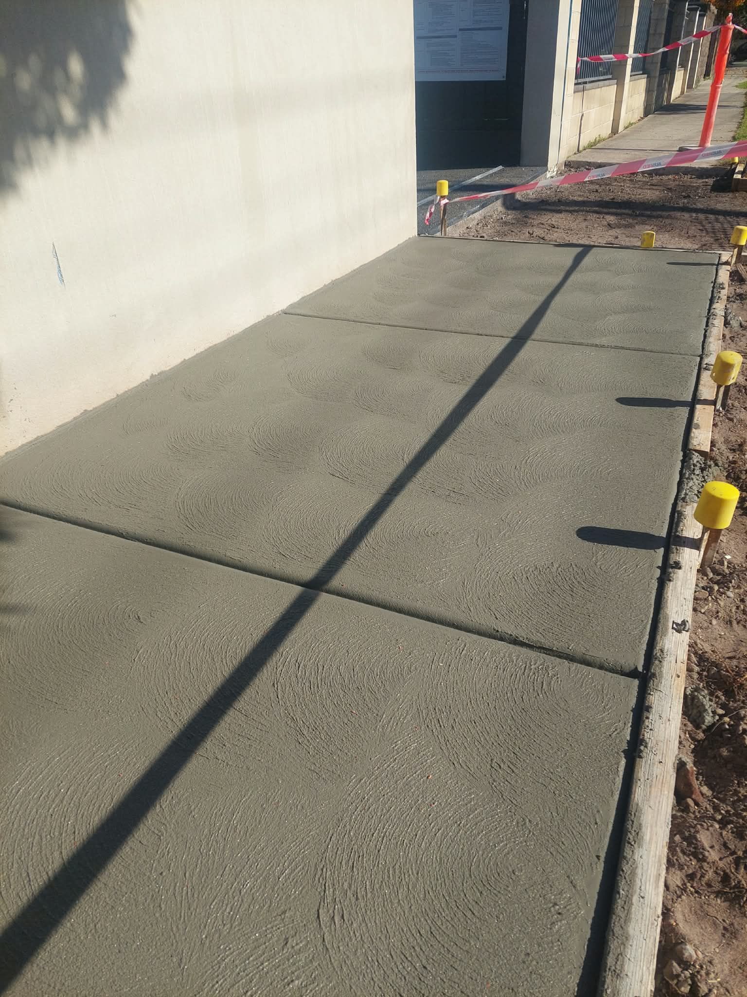 Concrete sidewalk beside a white wall, with cracks and a narrow landscaped edge on the right.