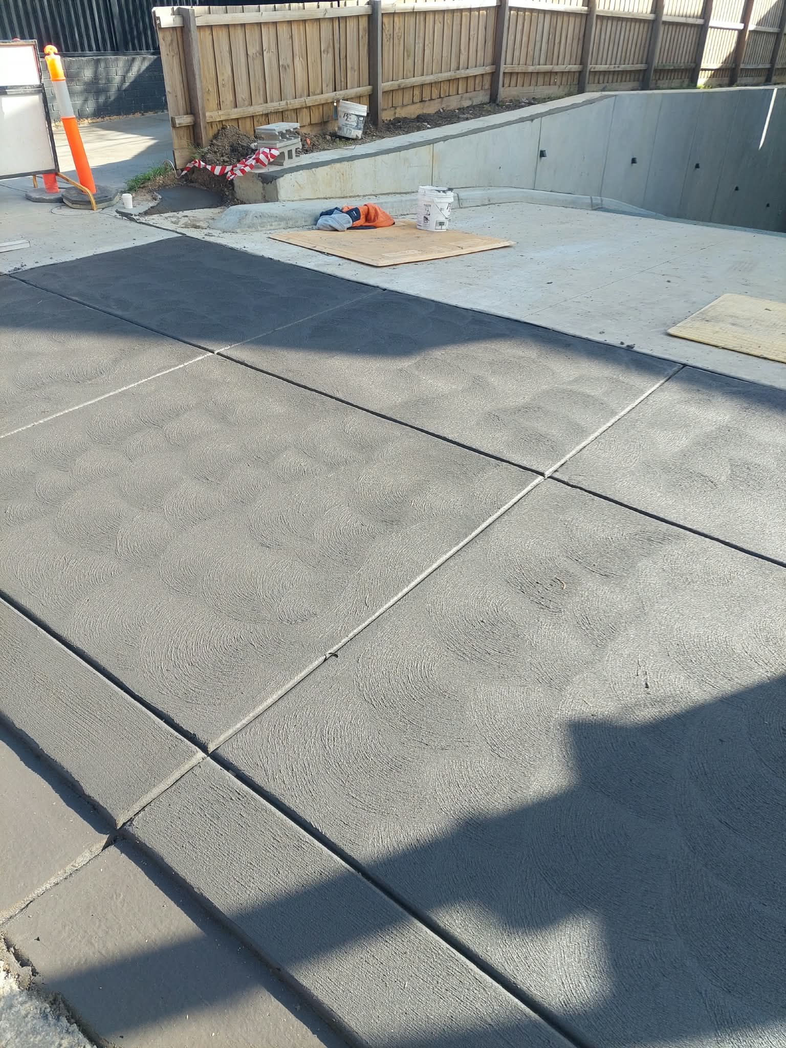 Concrete walkway beside a construction site with traffic cones, fencing, and a long shadow in the foreground