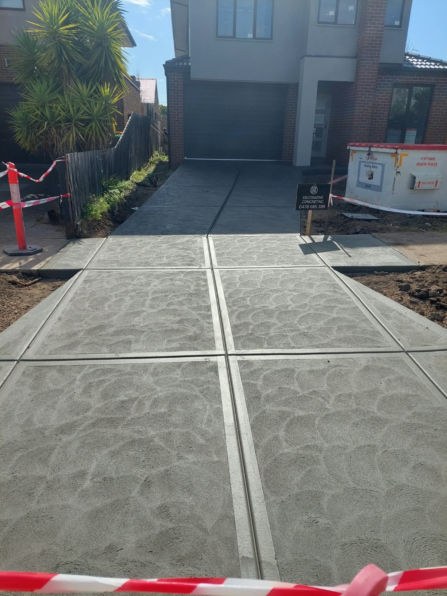 Fresh concrete driveway and walkway leading to a house, with construction barriers and a utility box on the right.