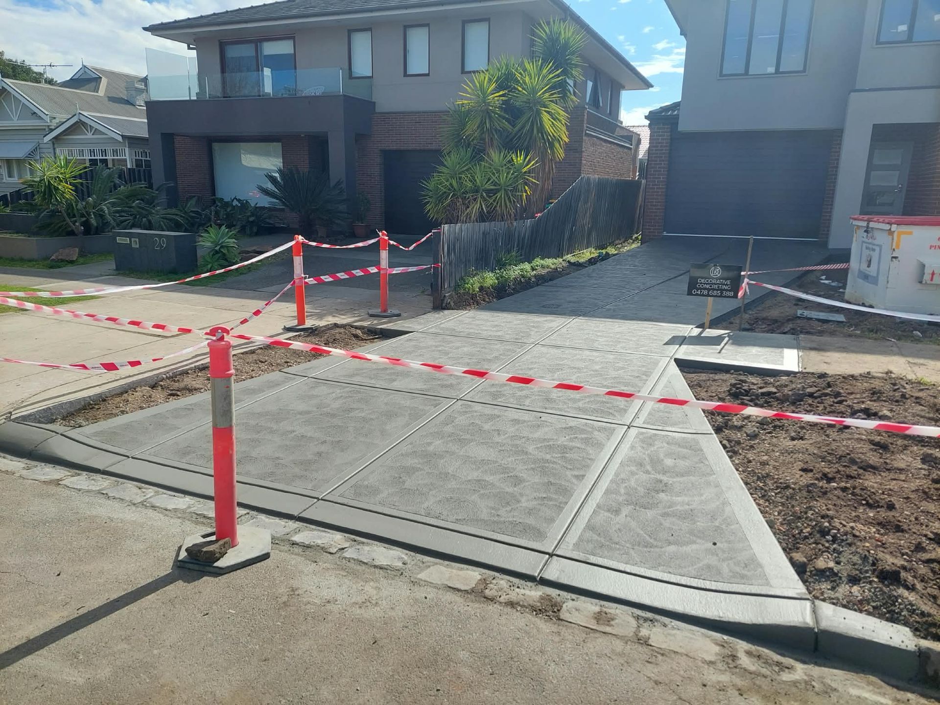 Curbside construction area with red caution tape blocking a new concrete driveway beside a house