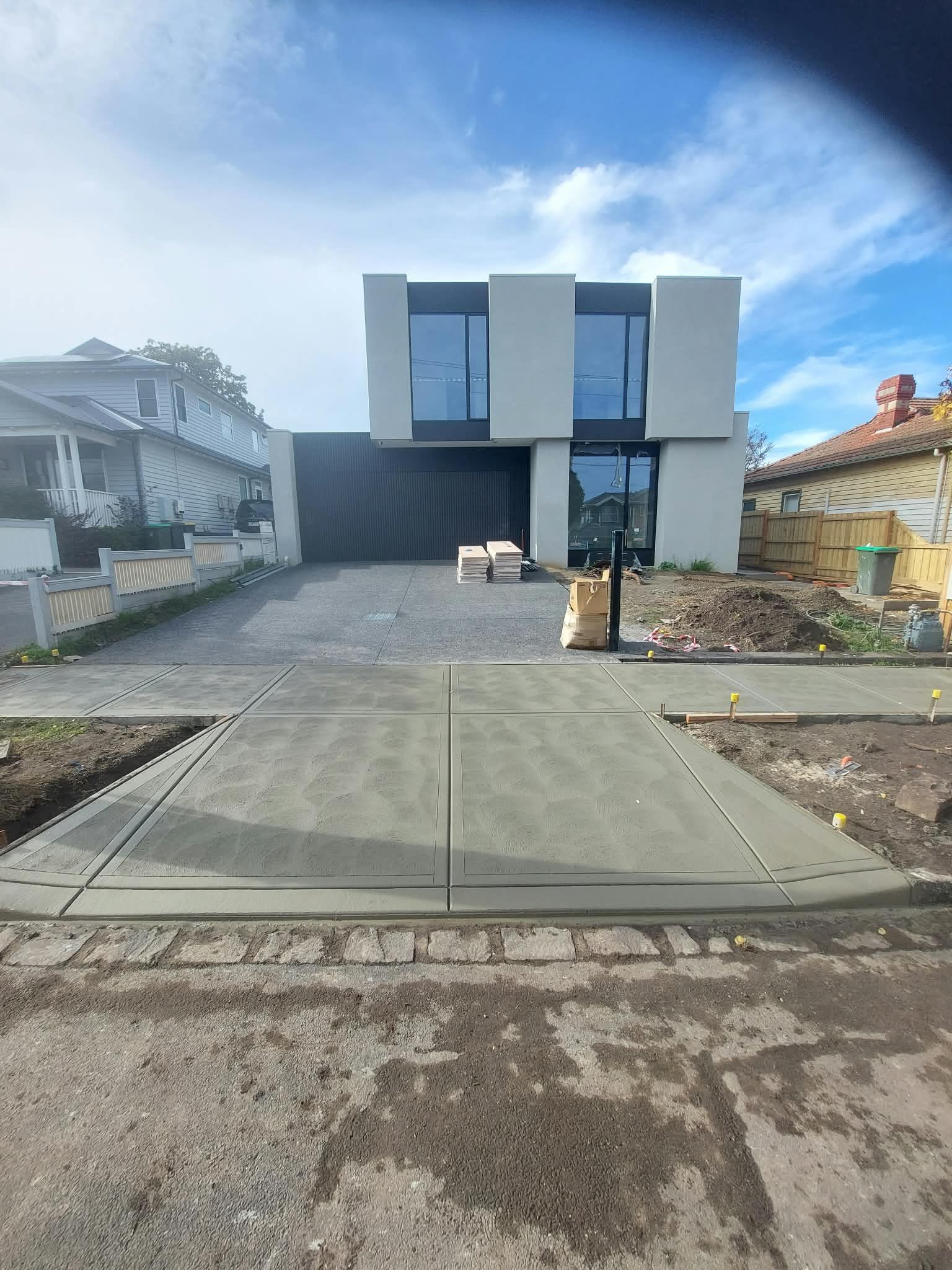 Modern house with a dark garage door, paved driveway, and cloudy sky on a residential street