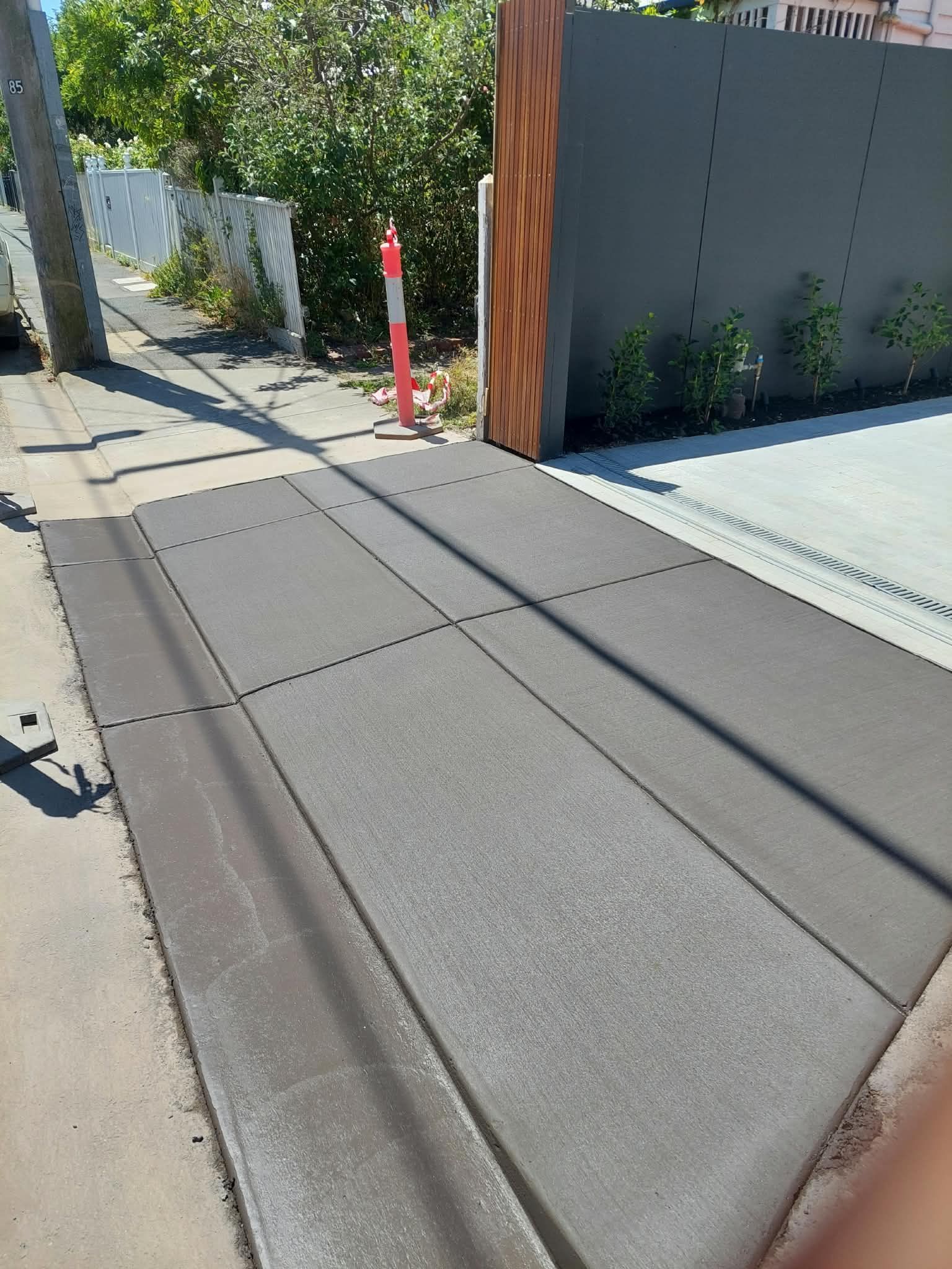 Sunlit sloped sidewalk beside a modern driveway gate and red bollard