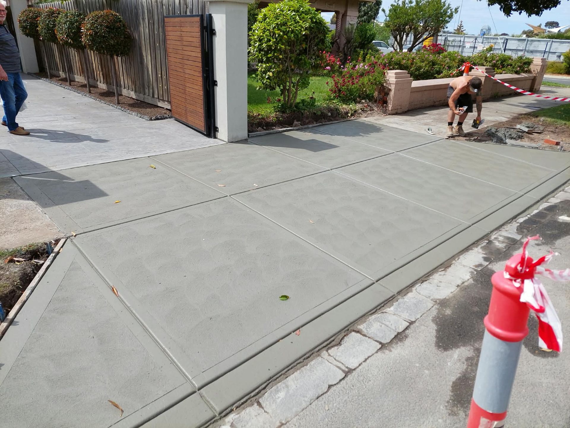 Sidewalk ramp beside a landscaped entrance, with a person on a bench and a small dog near the path.