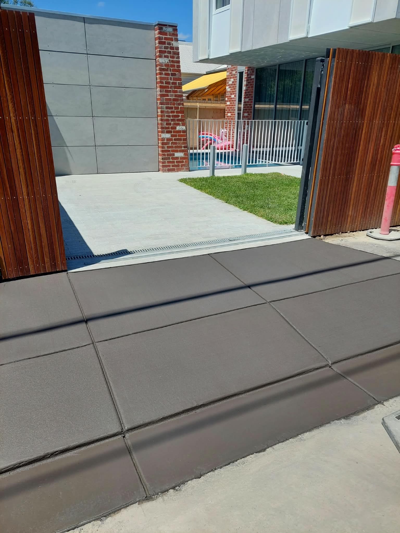 Accessible courtyard entrance with gray paving, brick pillars, and a metal gate beside a grassy area