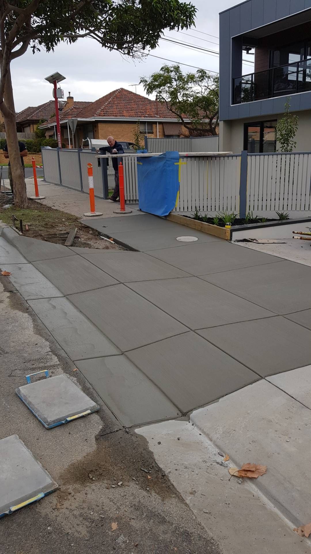 Sidewalk beside a construction fence with orange cones and a blue tarp in a residential street.