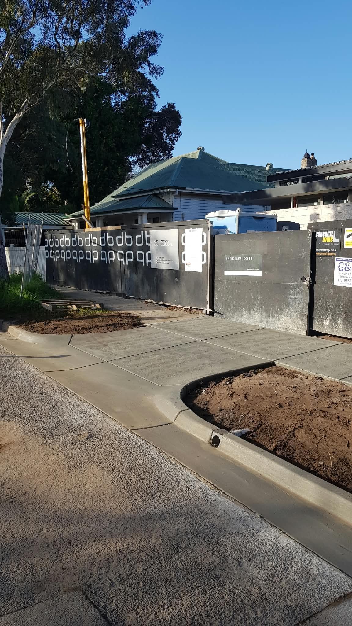 Residential construction site with gray fence, parked vehicle, and newly poured curb under a clear blue sky