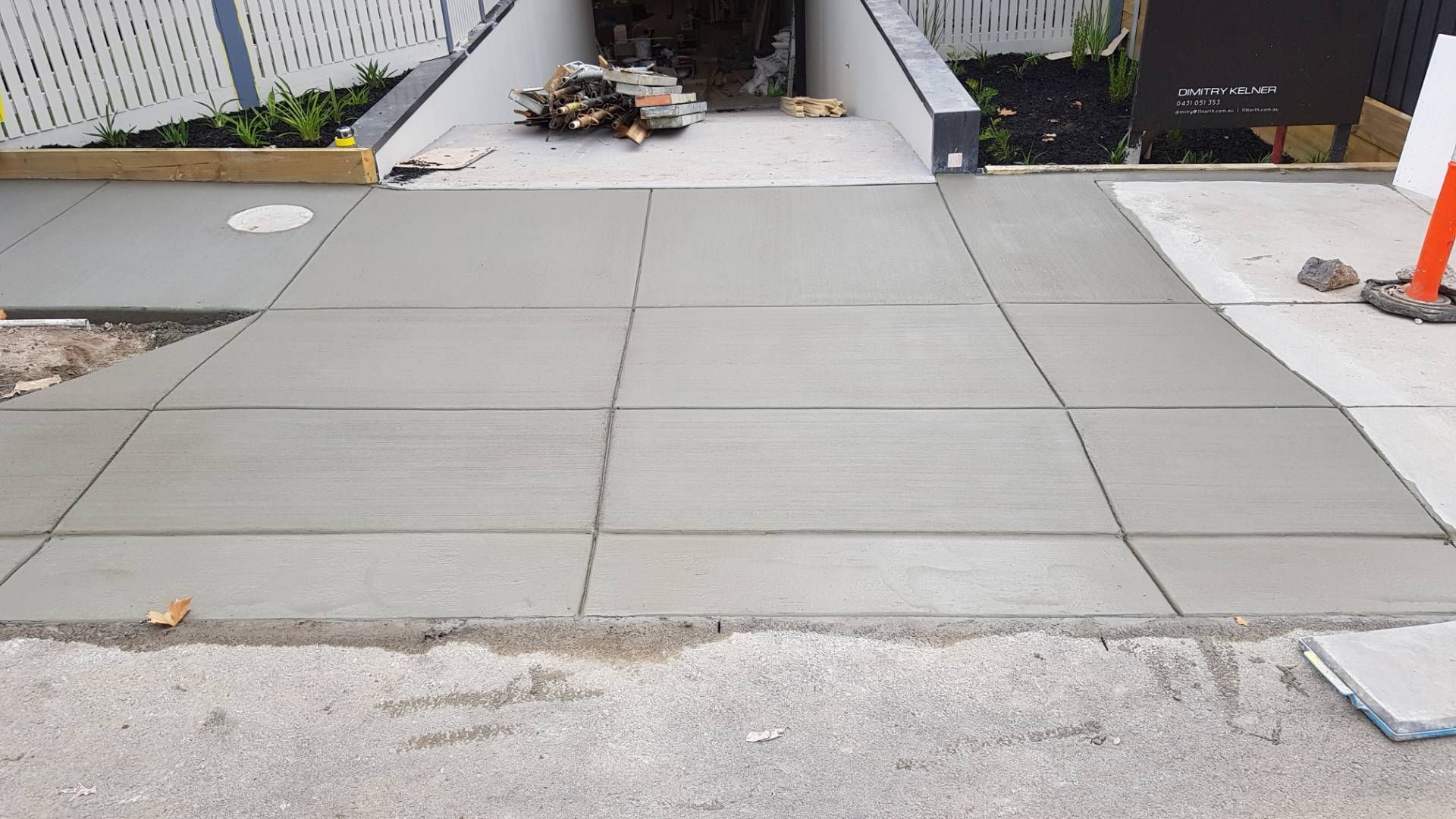 Freshly laid gray concrete driveway and sidewalk in front of a house under construction