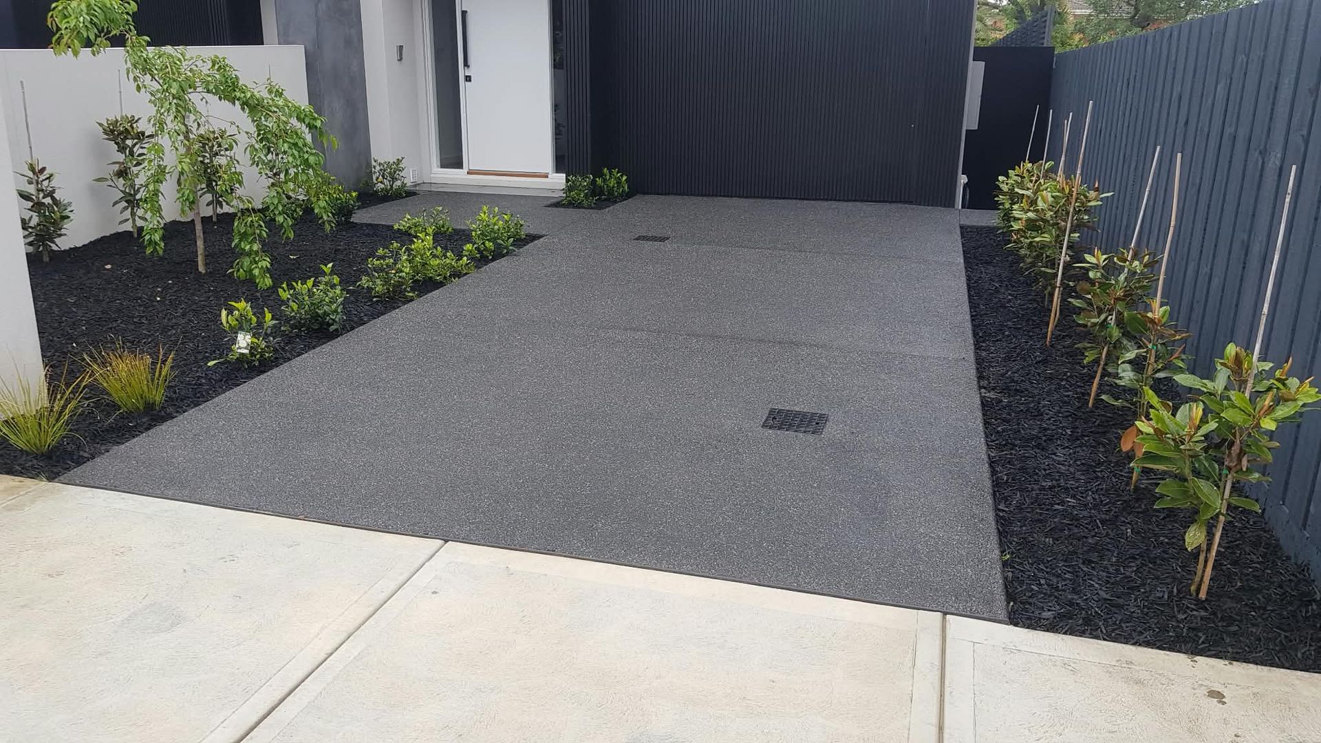 Modern house driveway with gray gravel, black mulch garden beds, and a concrete sidewalk in front