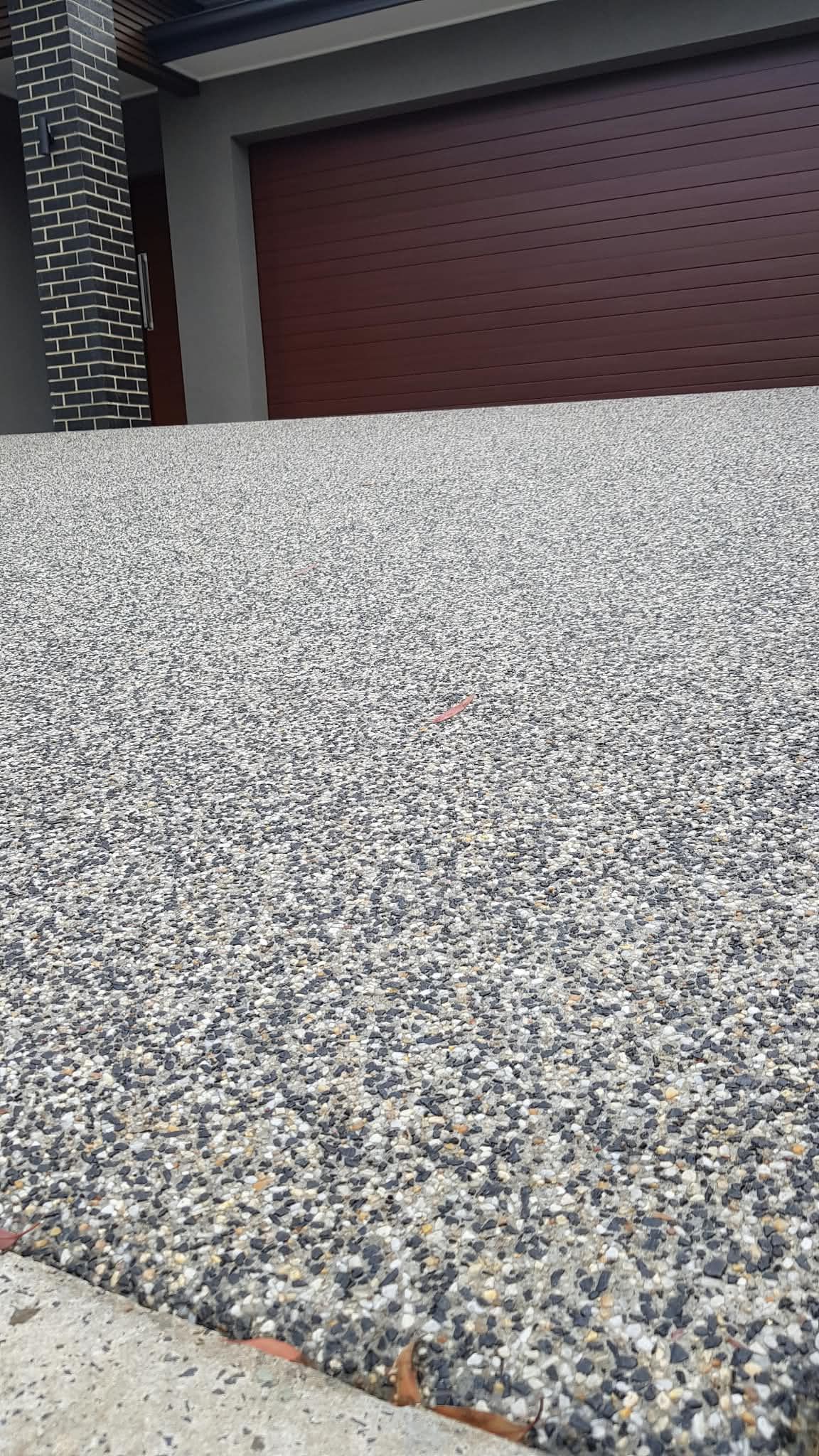 Gravel driveway leading to a maroon garage door beside a house wall