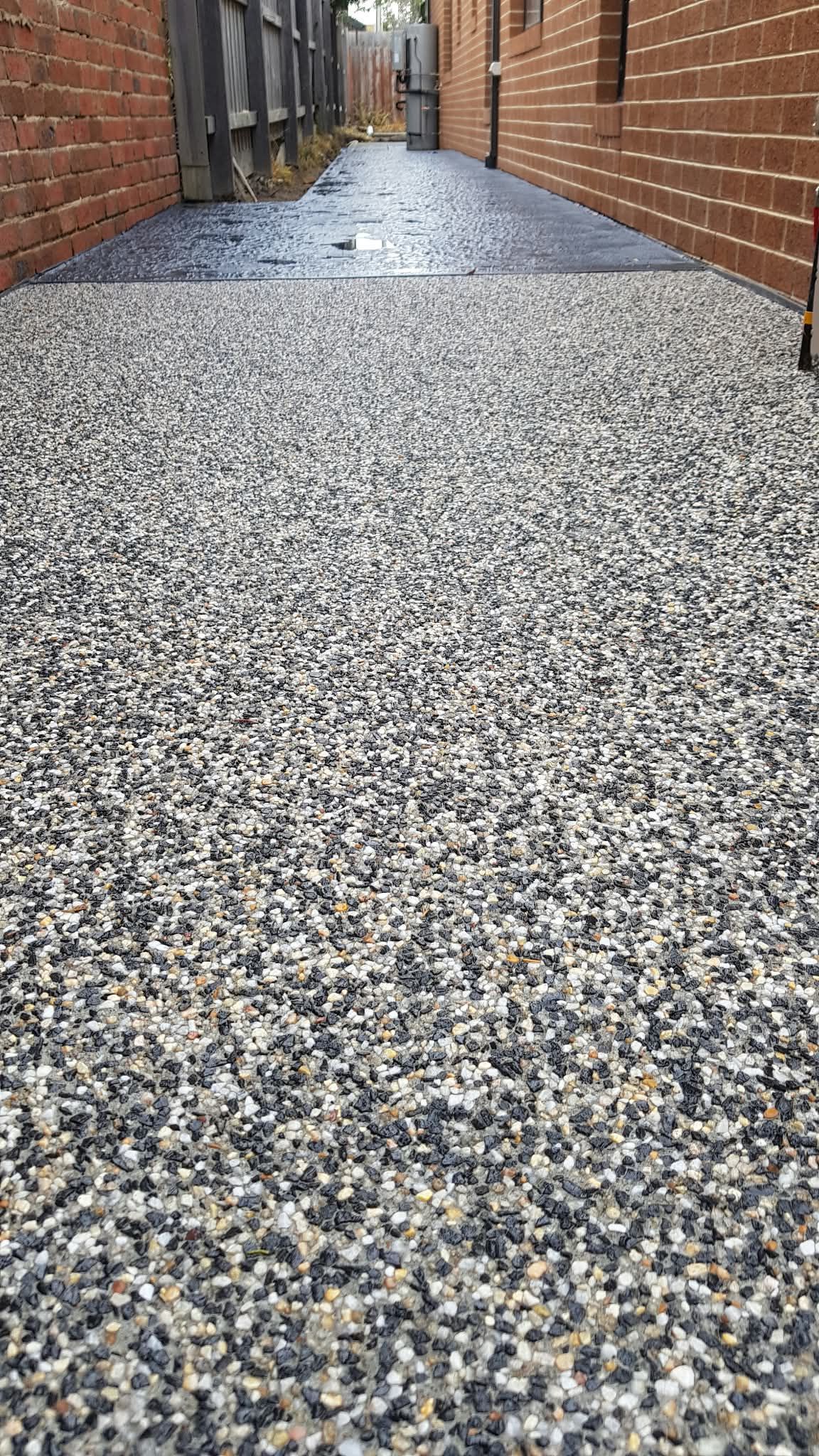 Pea gravel walkway between brick buildings, with wet pavement and a narrow path ahead