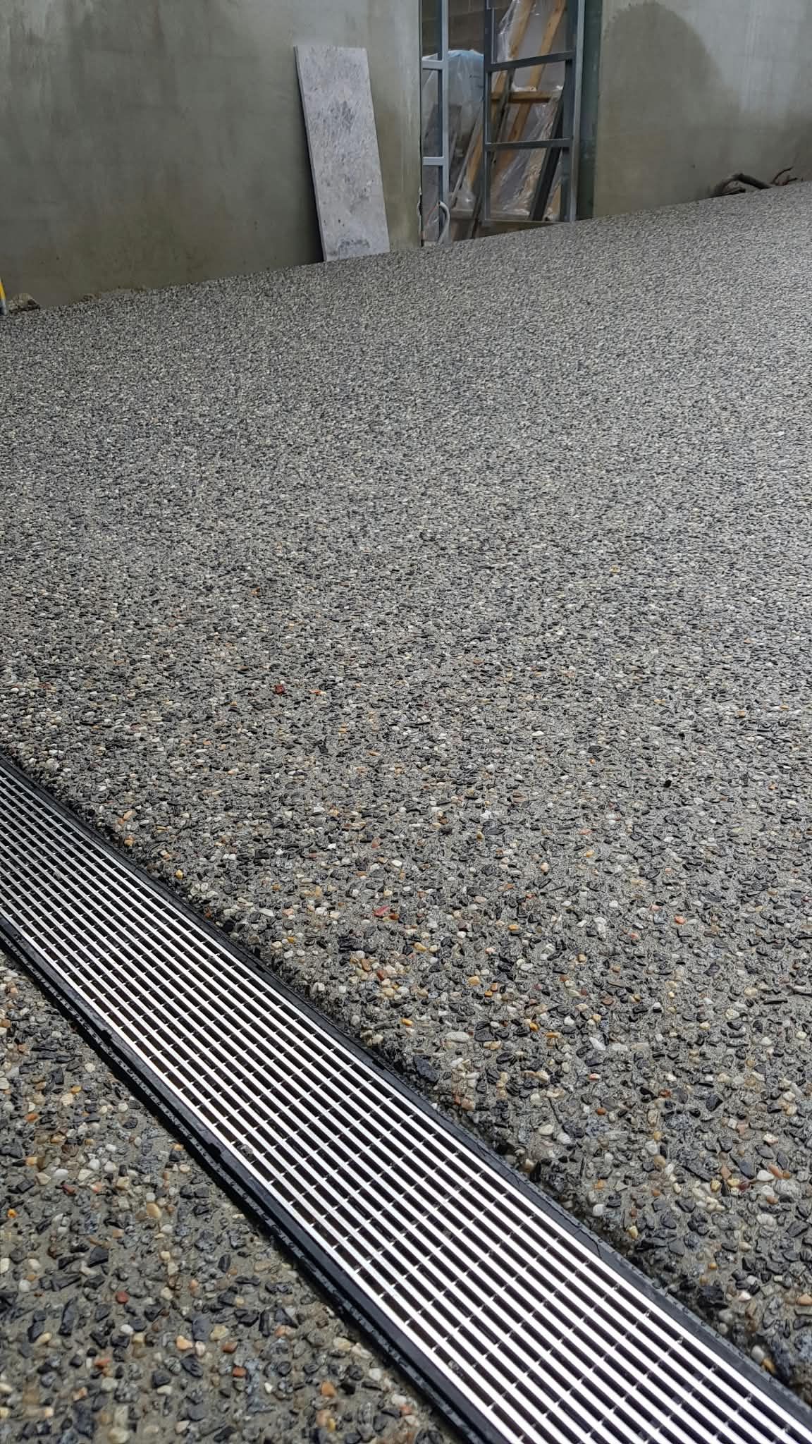 Small gray-and-black gravel surface beside a concrete wall and metal drainage grate indoors