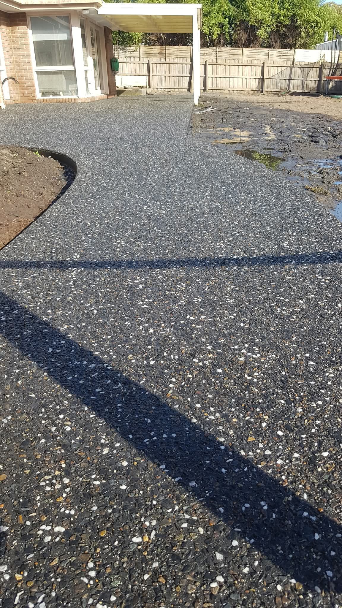Gravel-covered driveway or yard beside a house, with a shadow stretching across the foreground.
