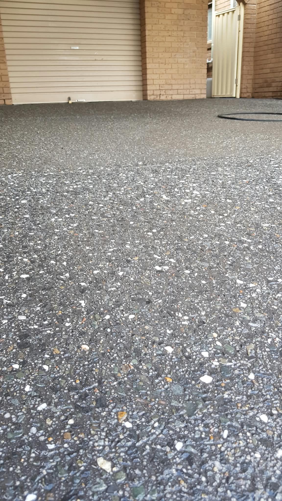 Low-angle view of a rough gravel driveway in front of a closed garage door and brick wall.