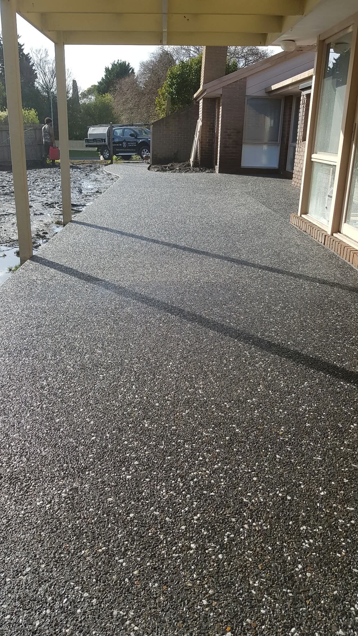 Covered gravel walkway beside a building, with parked vehicle and trees in the distance.