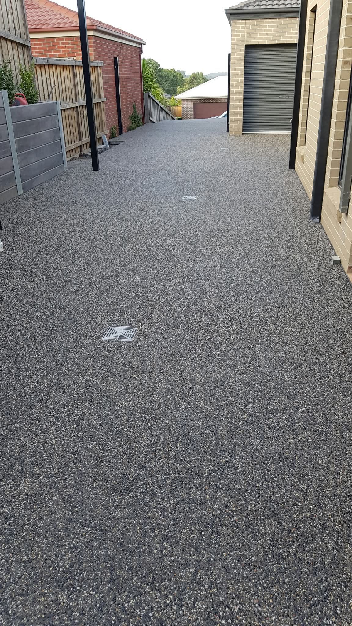 Gravel driveway beside brick homes and a garage with a metal roller door
