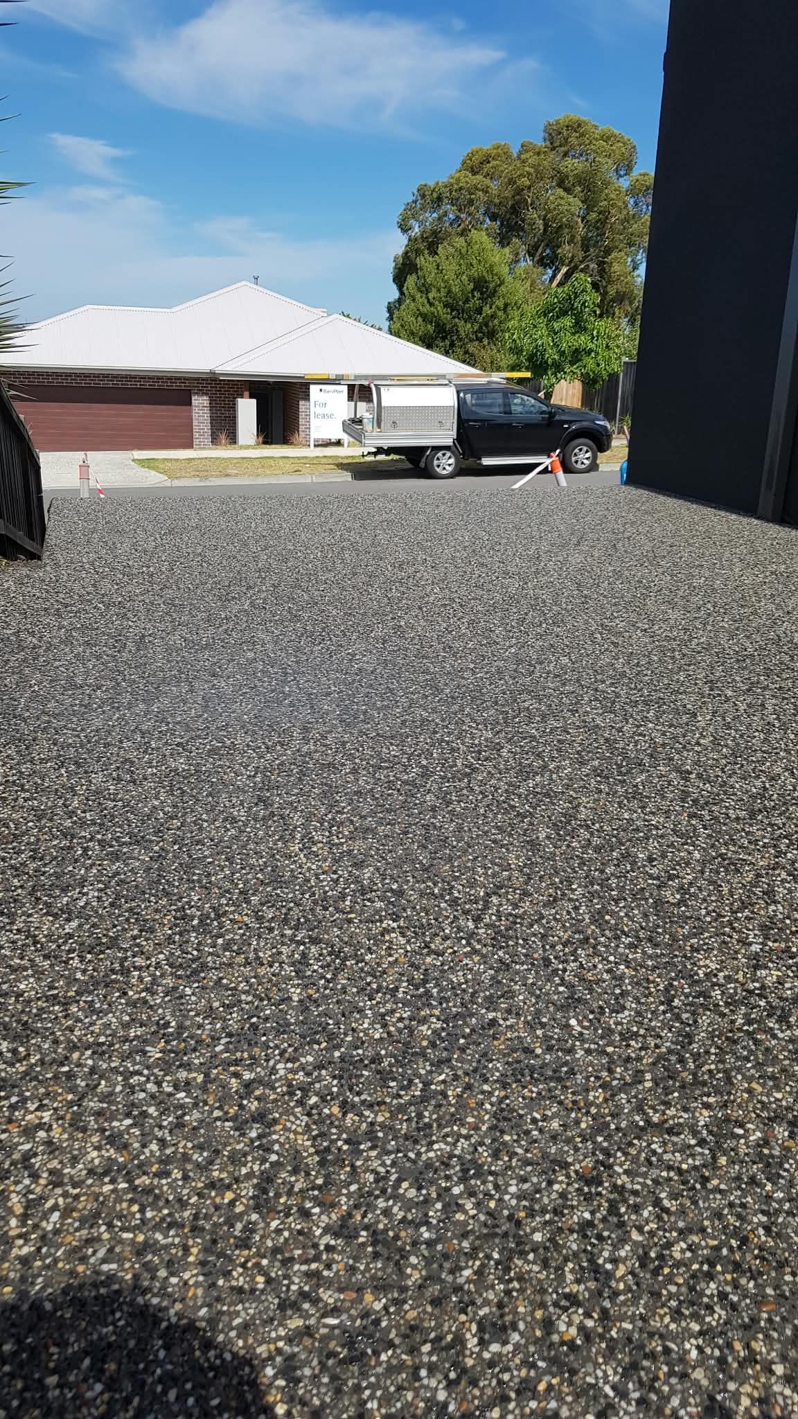 Gravel driveway beside a house with a parked black truck and blue sky