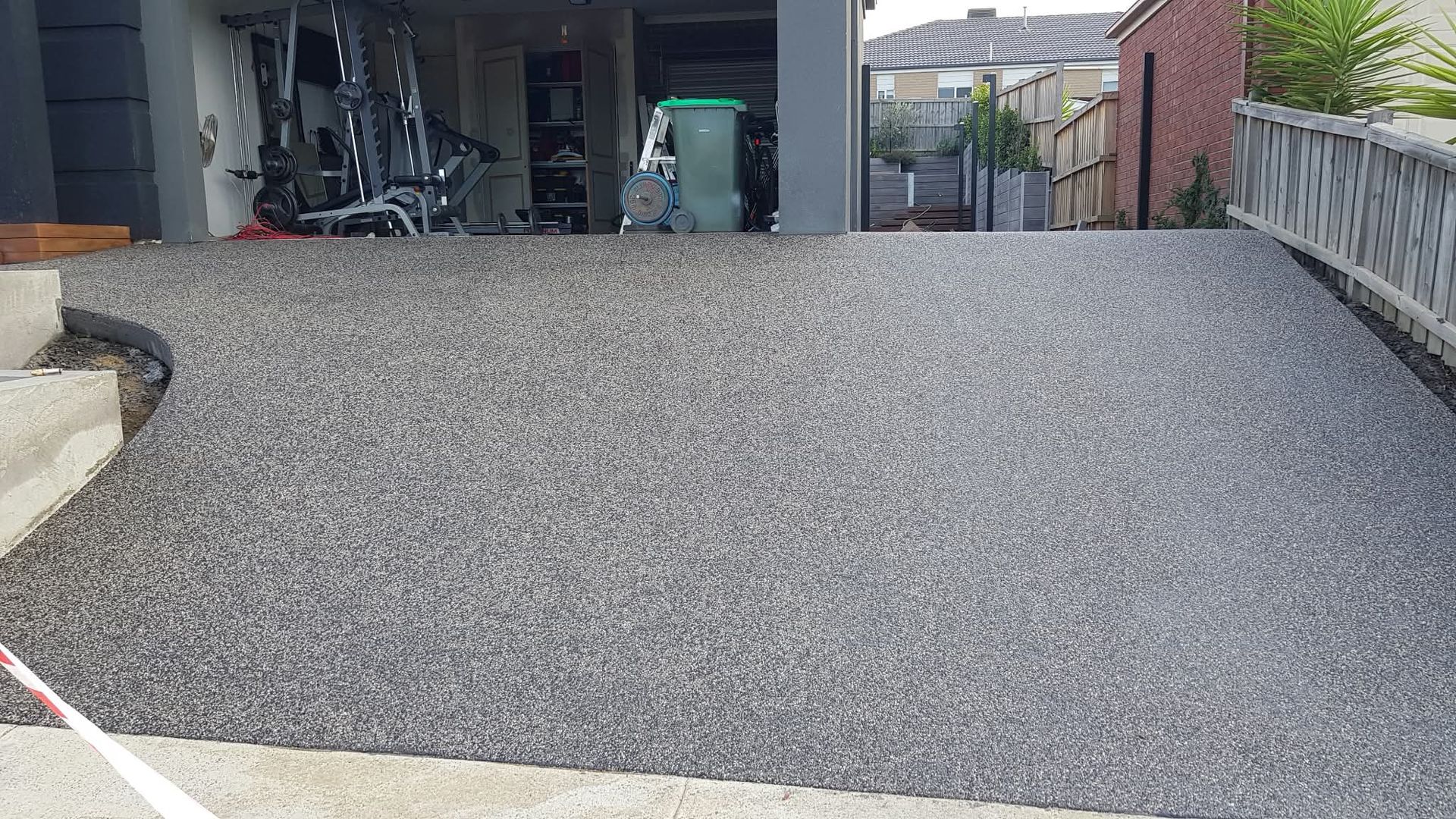 Gravel driveway ramp leading to a garage, with a railing on the right and a garden bed on the left