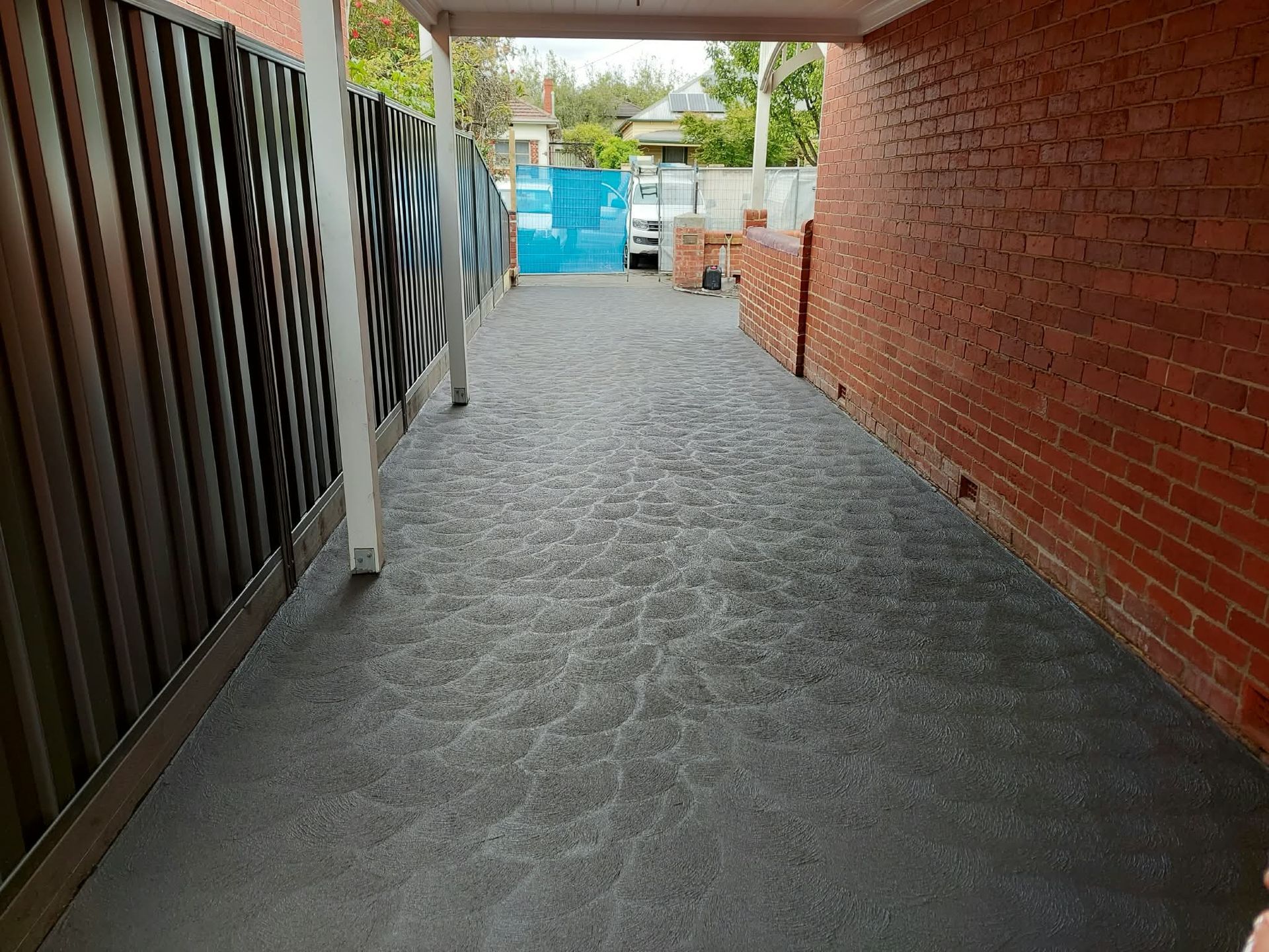 Narrow covered walkway with red brick wall, metal fence, and blue gate at the end