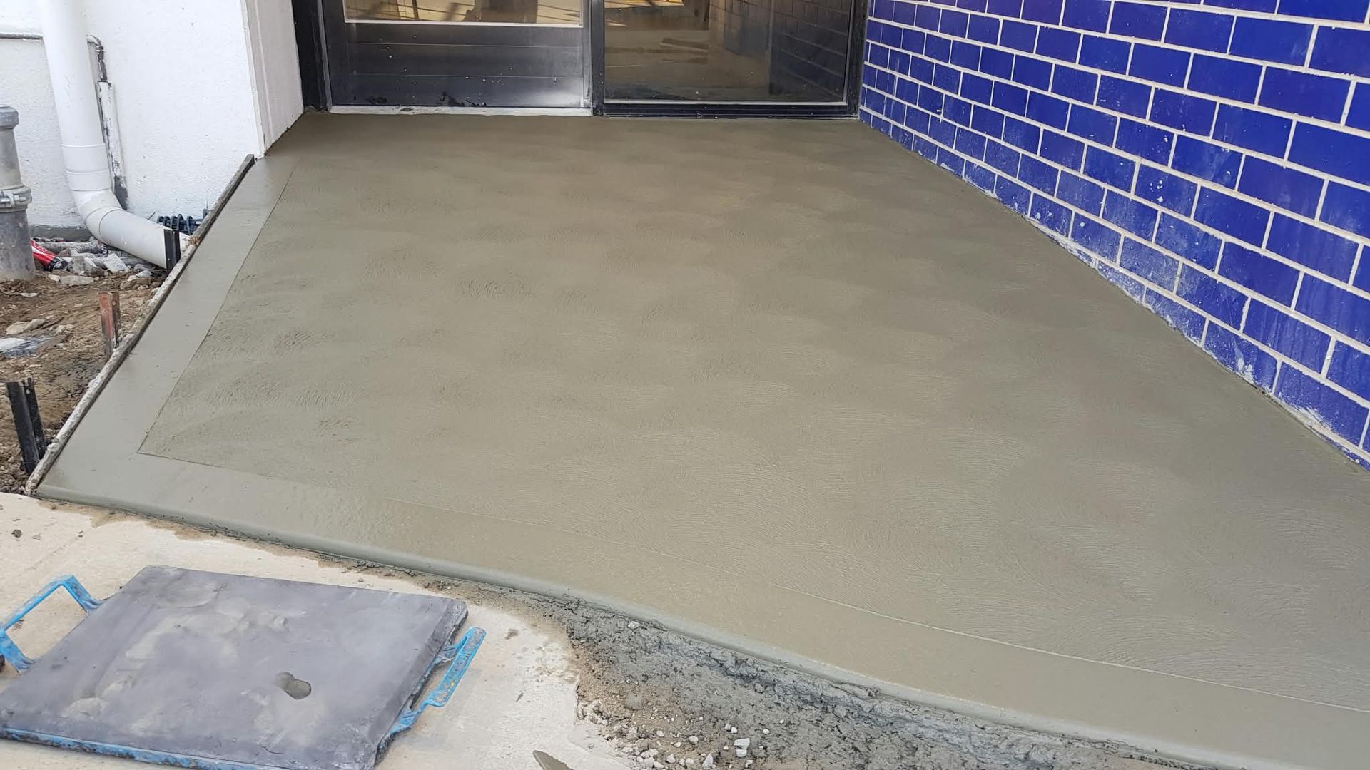 Freshly poured concrete ramp leading to a doorway beside a blue brick wall