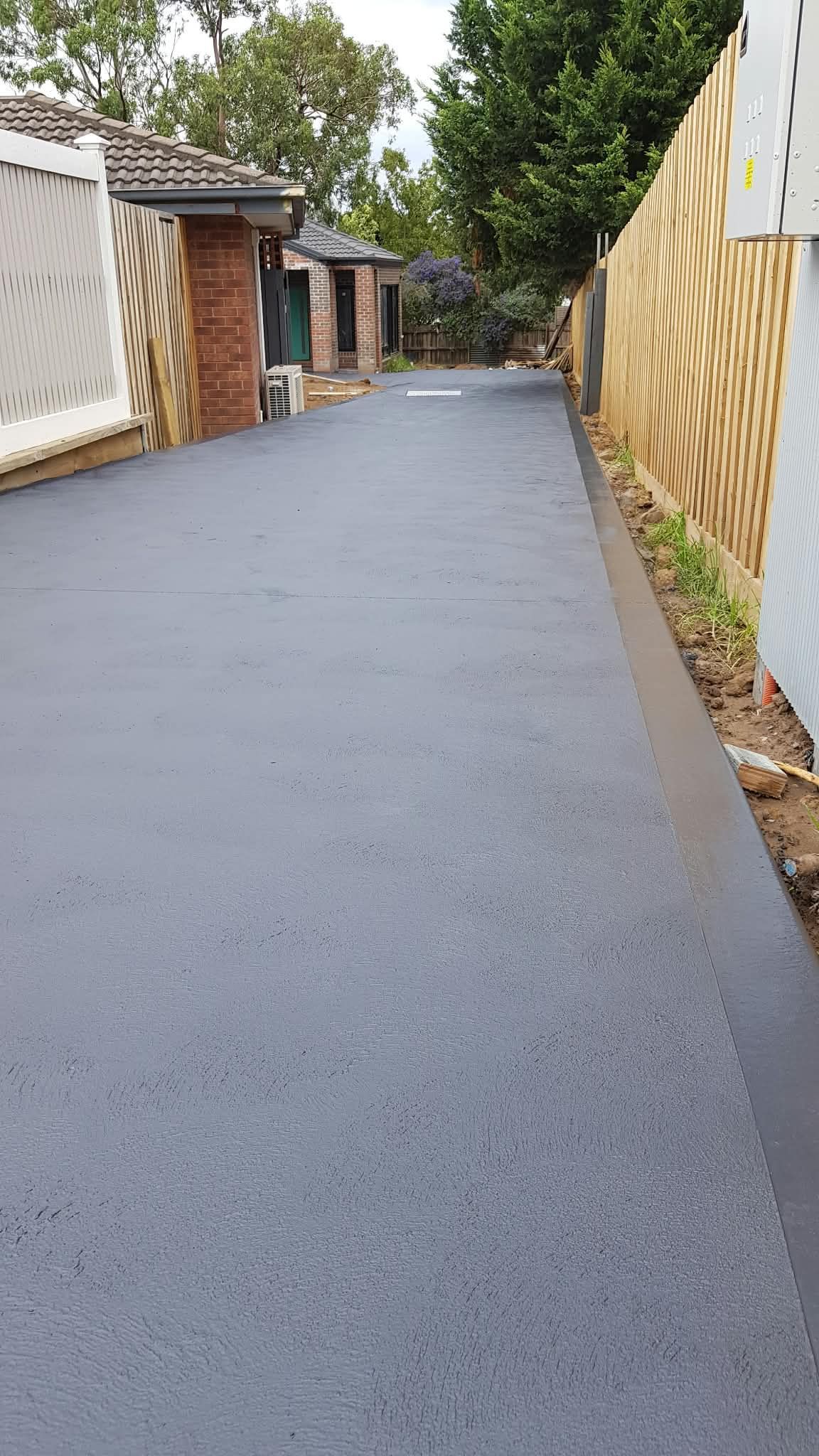 Freshly paved narrow driveway between houses with wooden fences and a zigzag pattern on the right