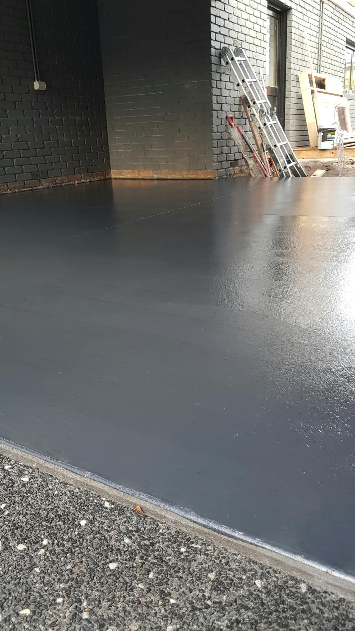 Freshly poured dark gray concrete beside a brick building, with scaffolding and tools in the background.