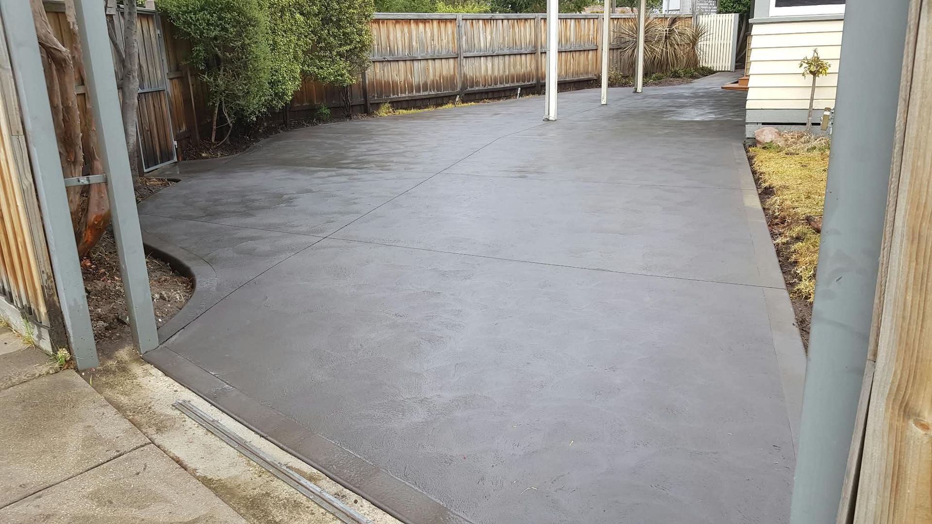 Freshly poured concrete patio or driveway between fences and a house in a backyard area