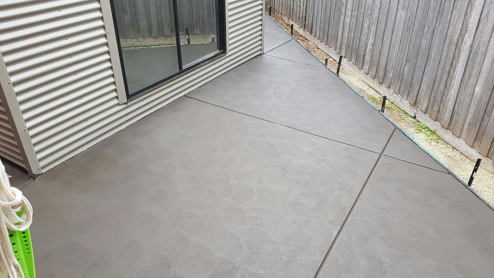 Gray concrete patio beside a house and wooden fence, with a sliding glass door.