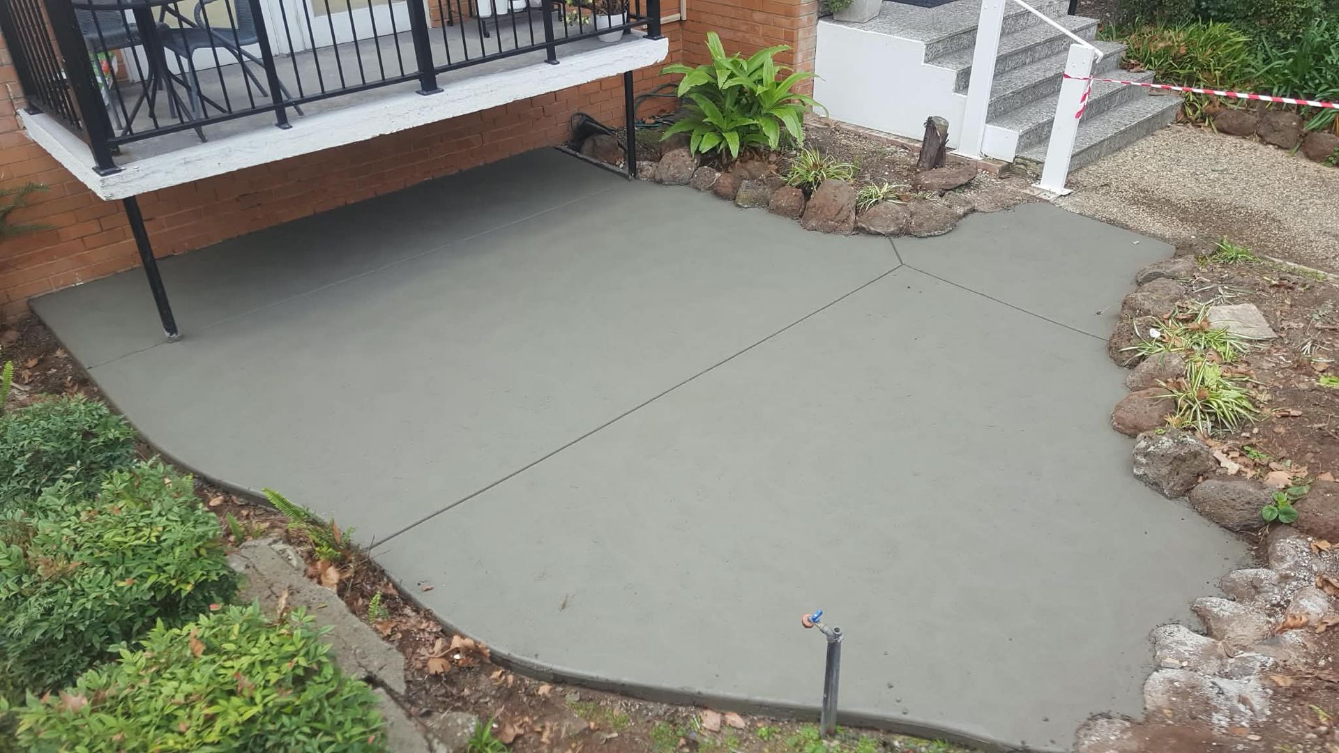 Freshly poured gray concrete patio bordered by landscaping and a deck railing