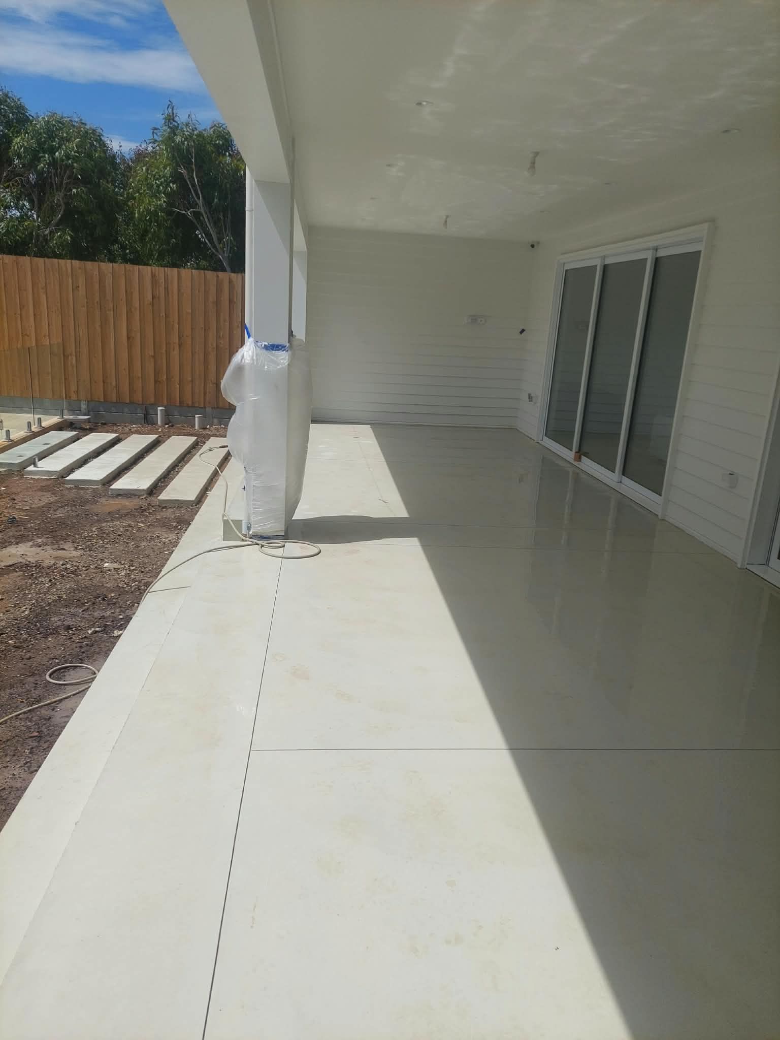 Covered patio with white floor, sliding glass doors, and a wooden fence beside a landscaped yard