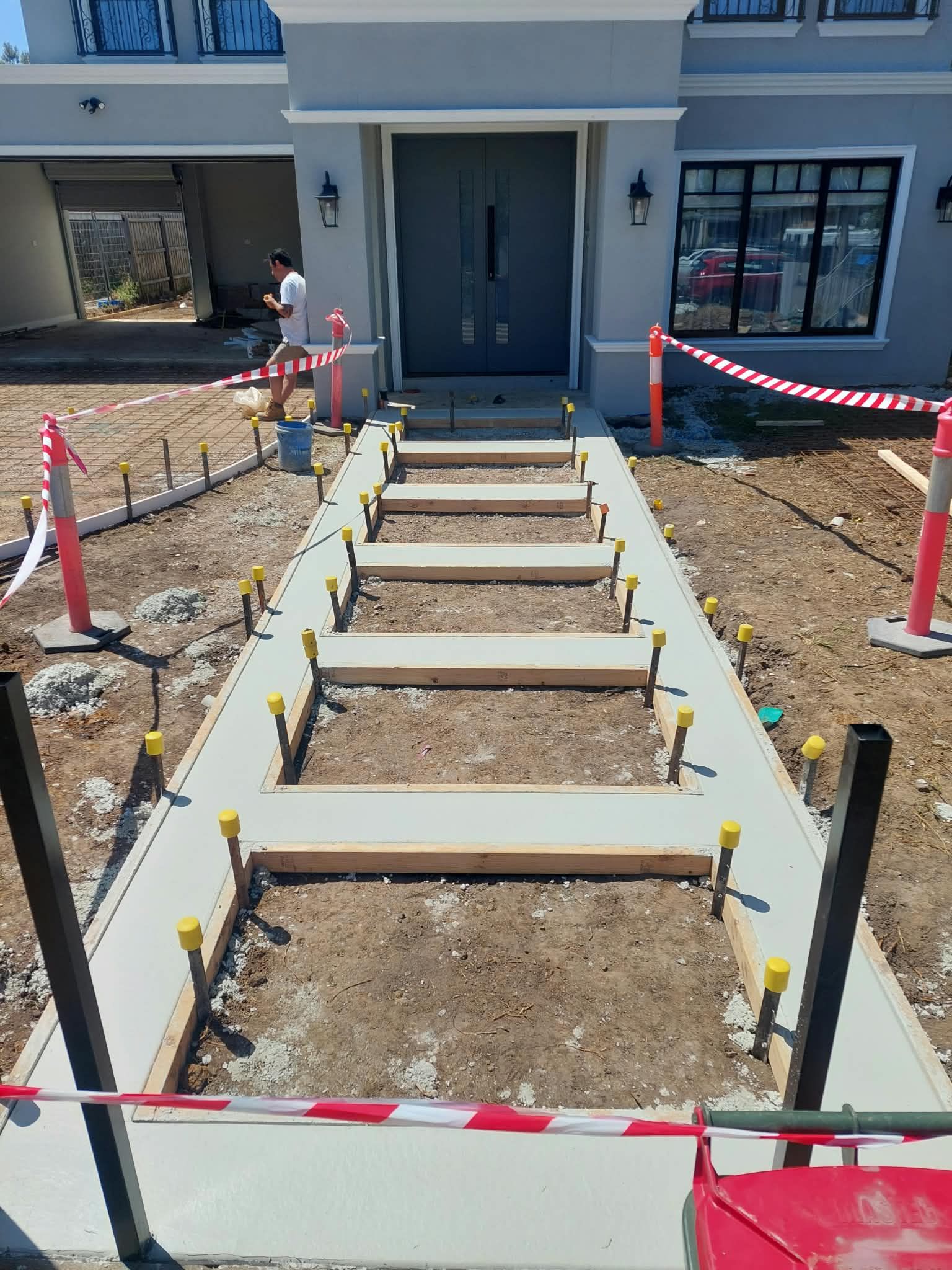 Front walkway under construction with concrete steps, dirt beds, and caution tape leading to a house entrance