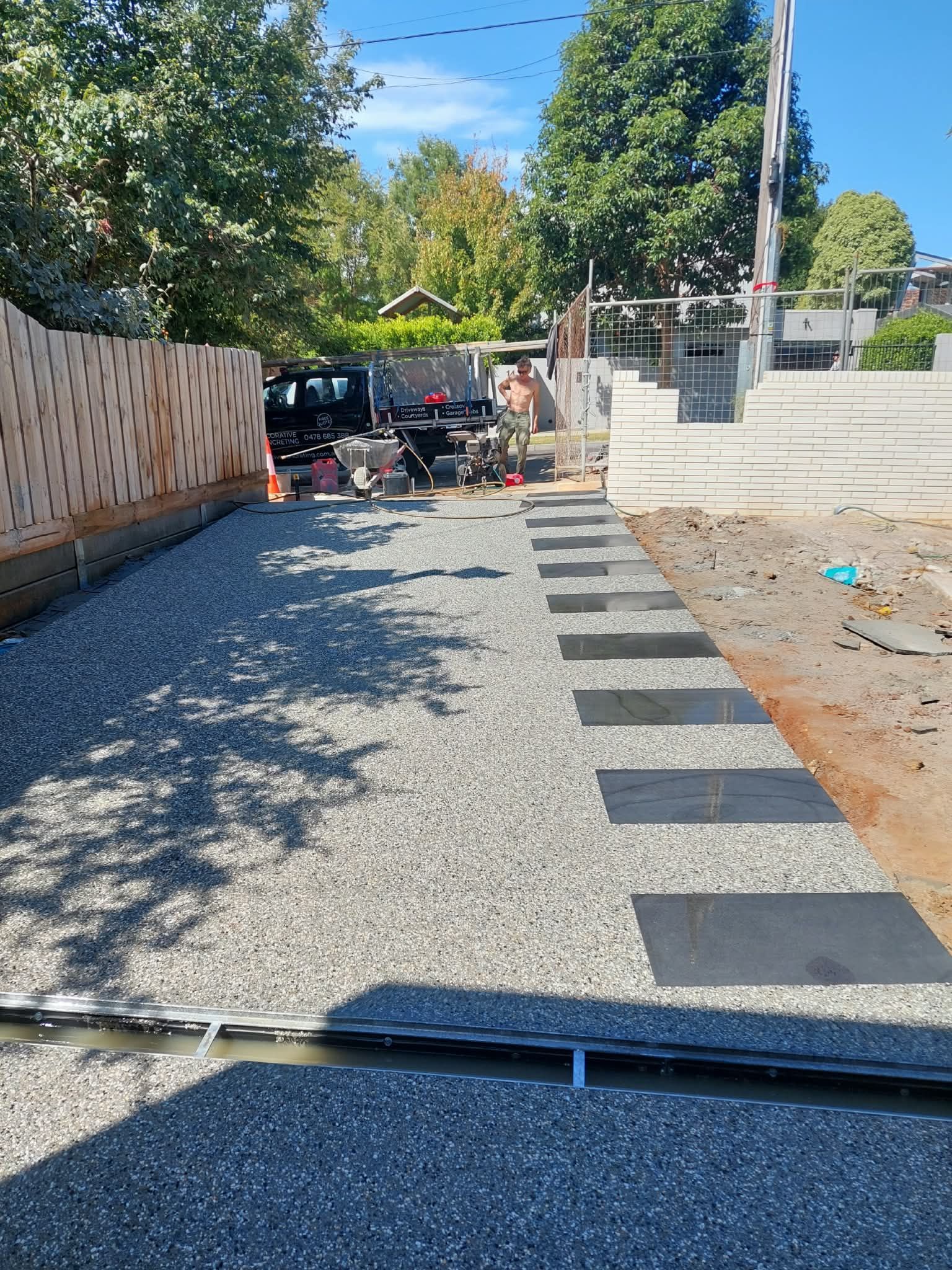 Gravel path under construction with pavers, fencing, and workers in a sunny residential street