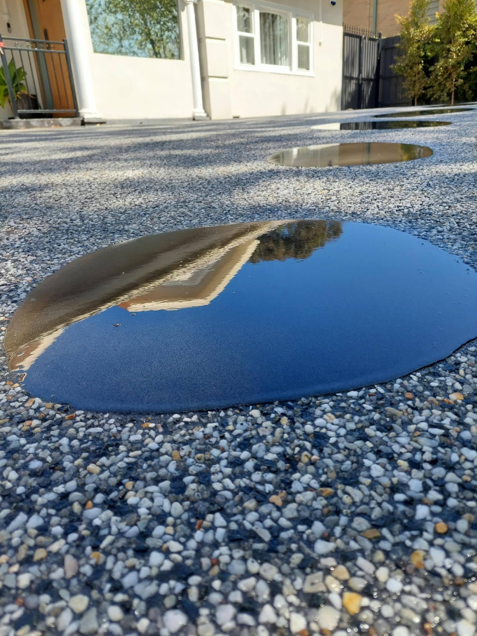 Puddle reflecting a building on a gravel-covered ground outside a house