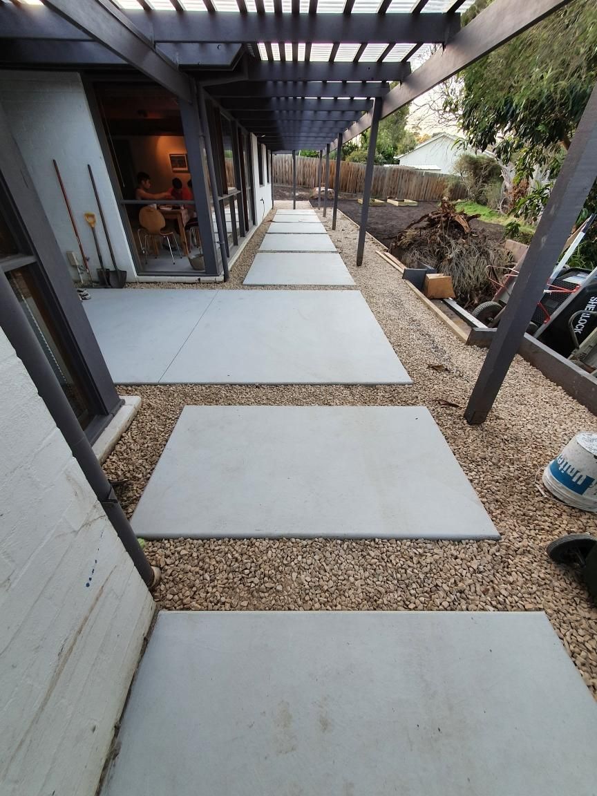 Backyard concrete stepping stones through gravel beside a covered patio